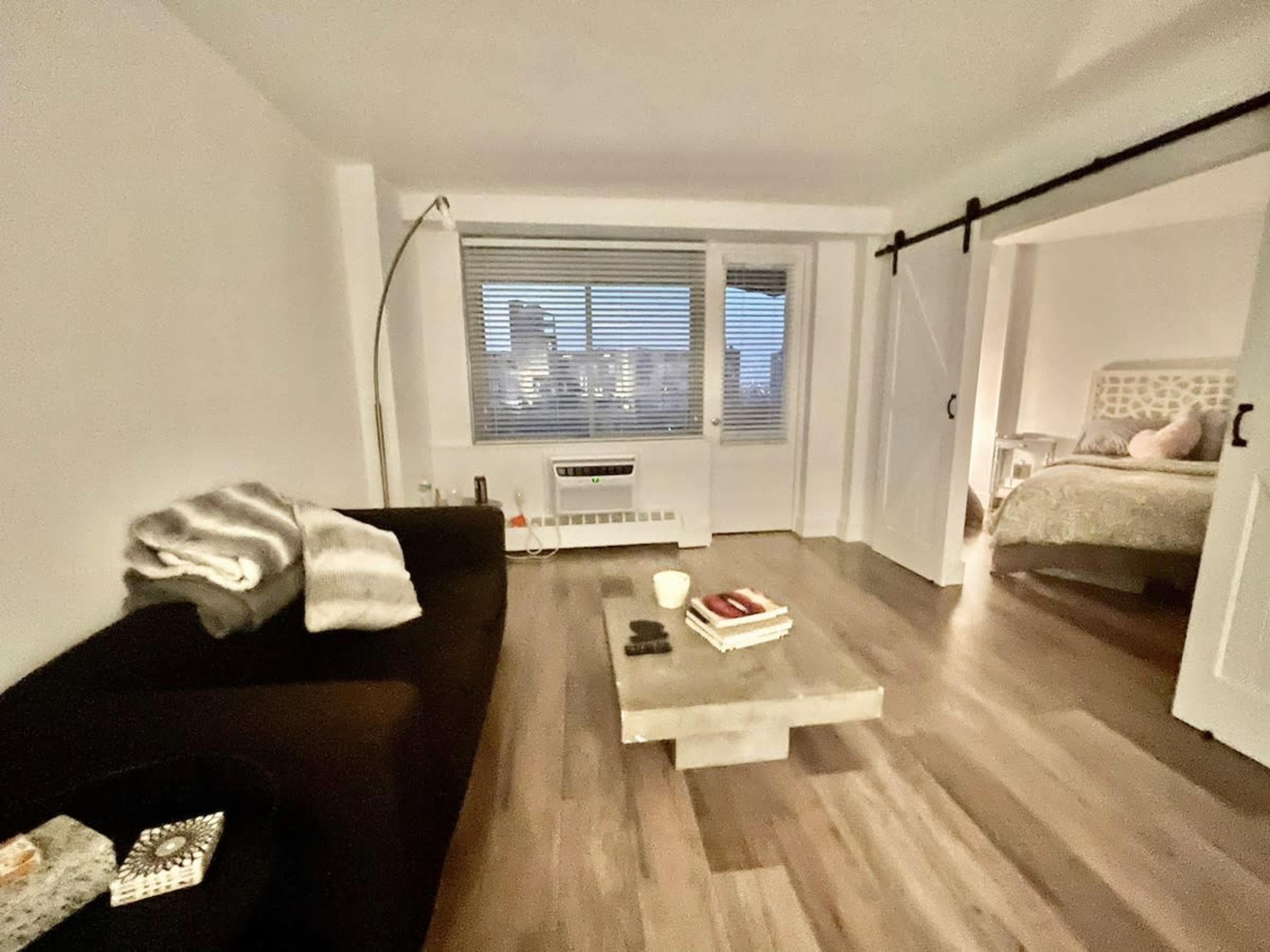A modern living space features a dark sofa, a coffee table with books, and large windows overlooking a city skyline.