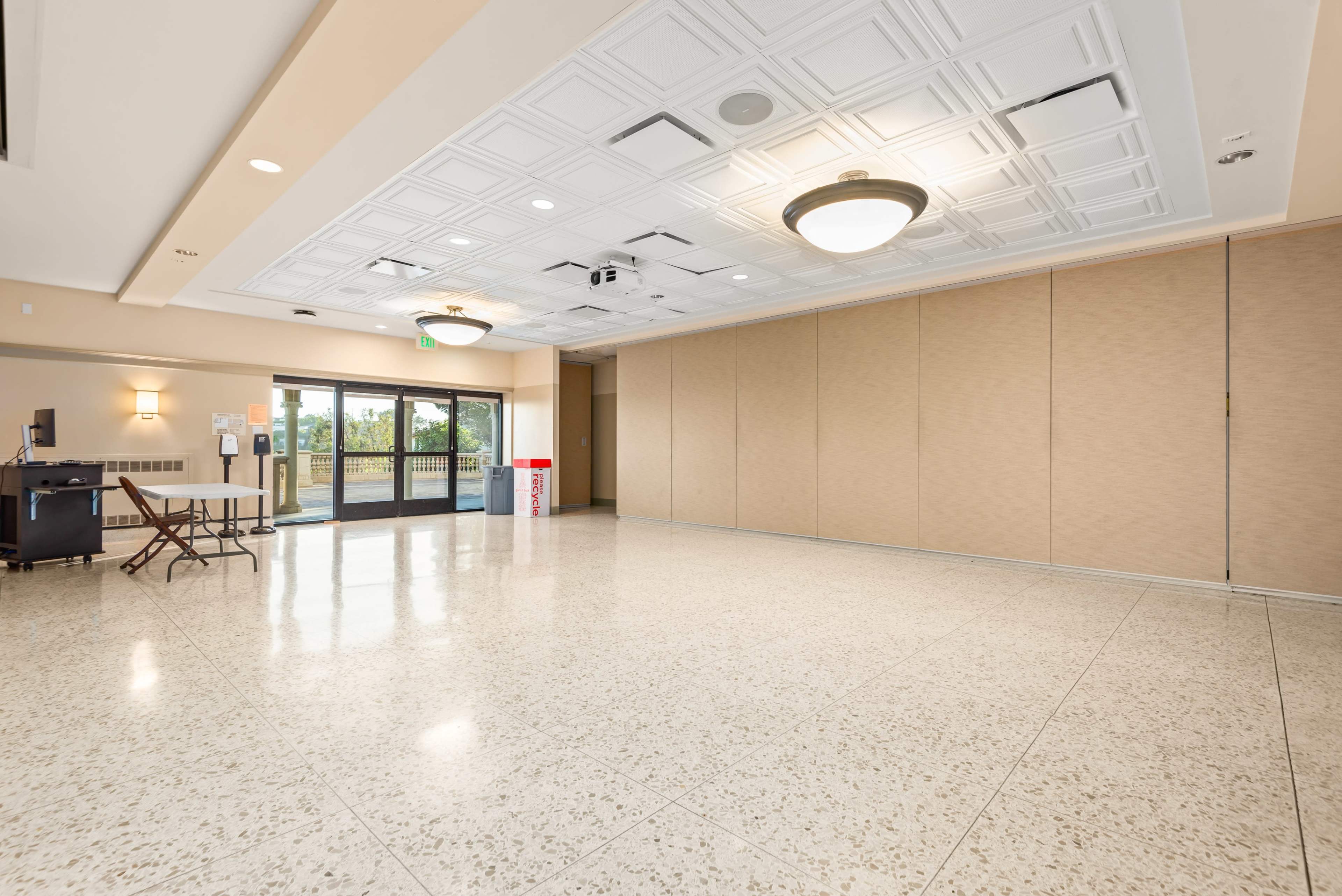 The image shows a spacious indoor room with a flat ceiling, light-colored walls, and a large entrance that opens to the outdoors.