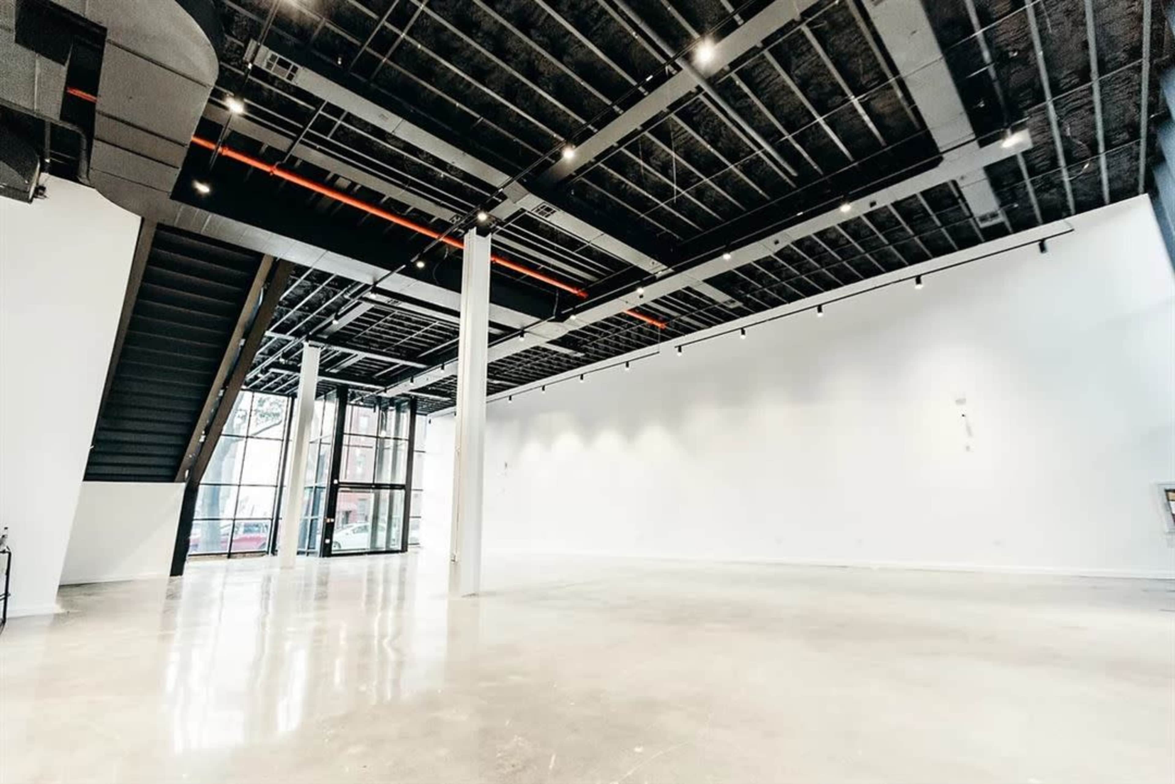 A spacious, empty interior of a modern building with a polished concrete floor, large windows, and an upper staircase.