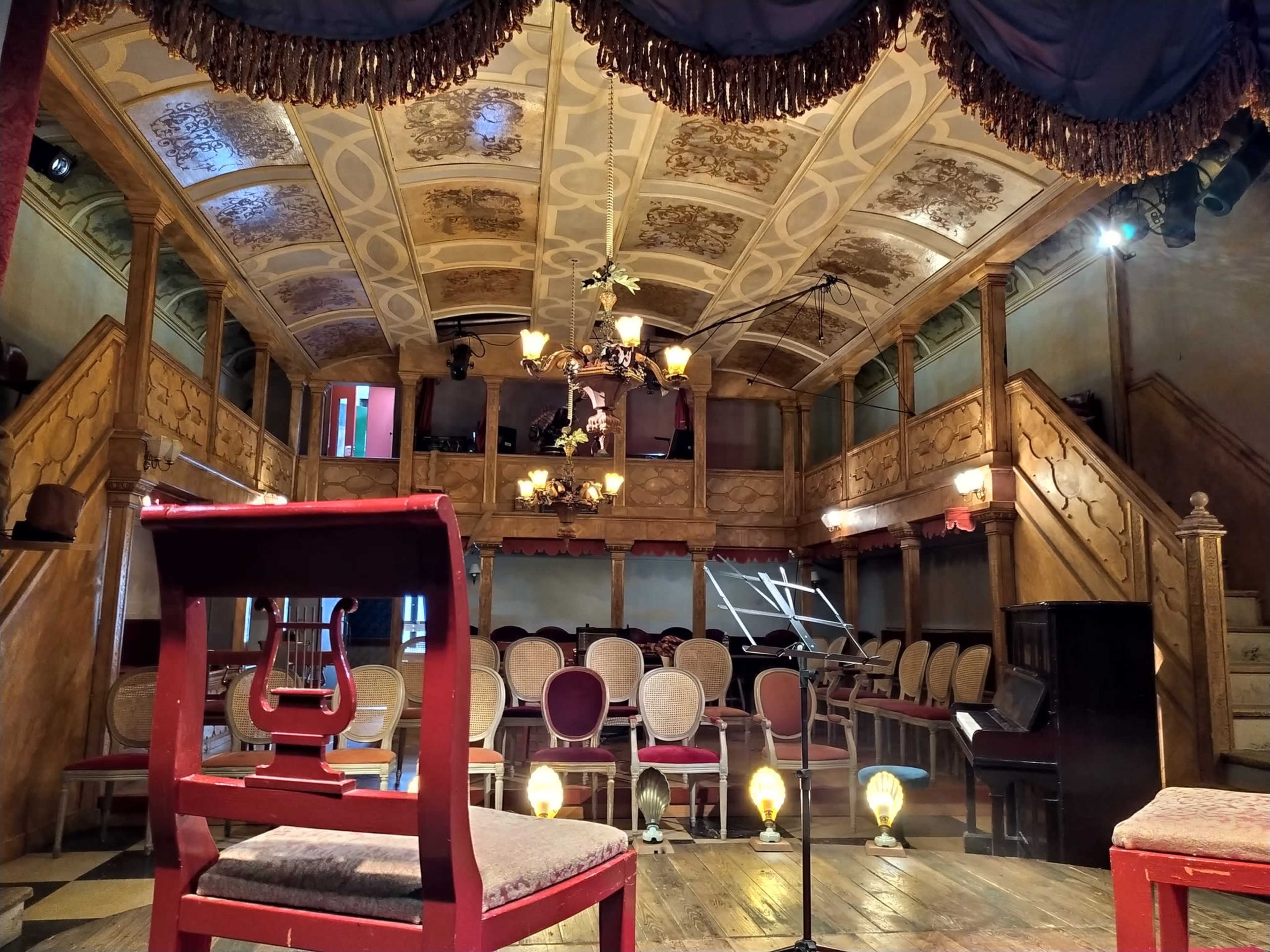 A vintage theater interior with a stage, ornate ceiling, and rows of chairs arranged in front of it.