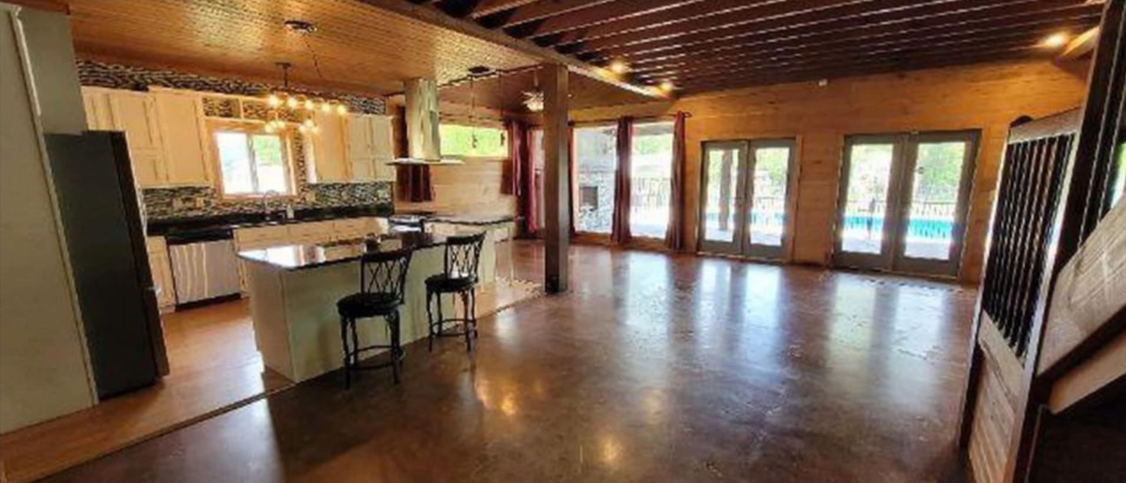 An open-concept living area with a kitchen, dining space, and large windows overlooking a pool.