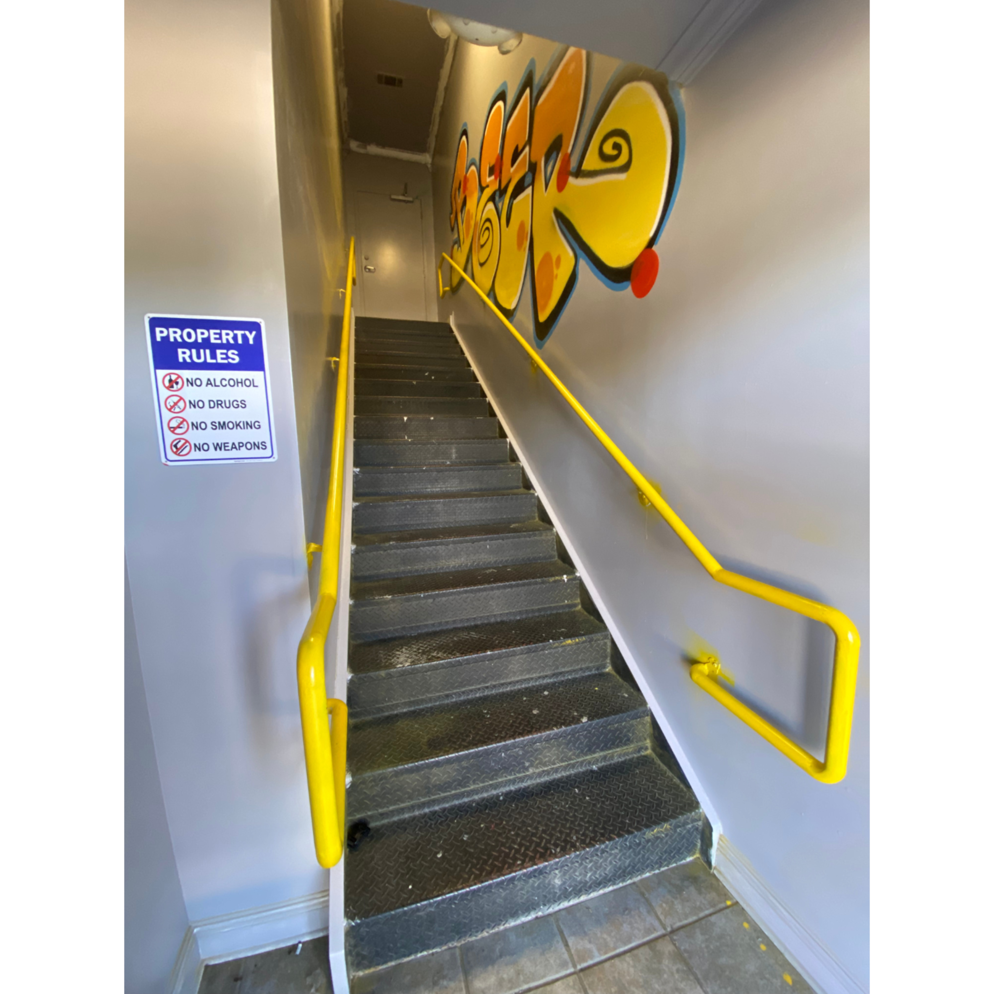 A set of metal stairs leads upward, flanked by a yellow railing and a wall featuring colorful graffiti.