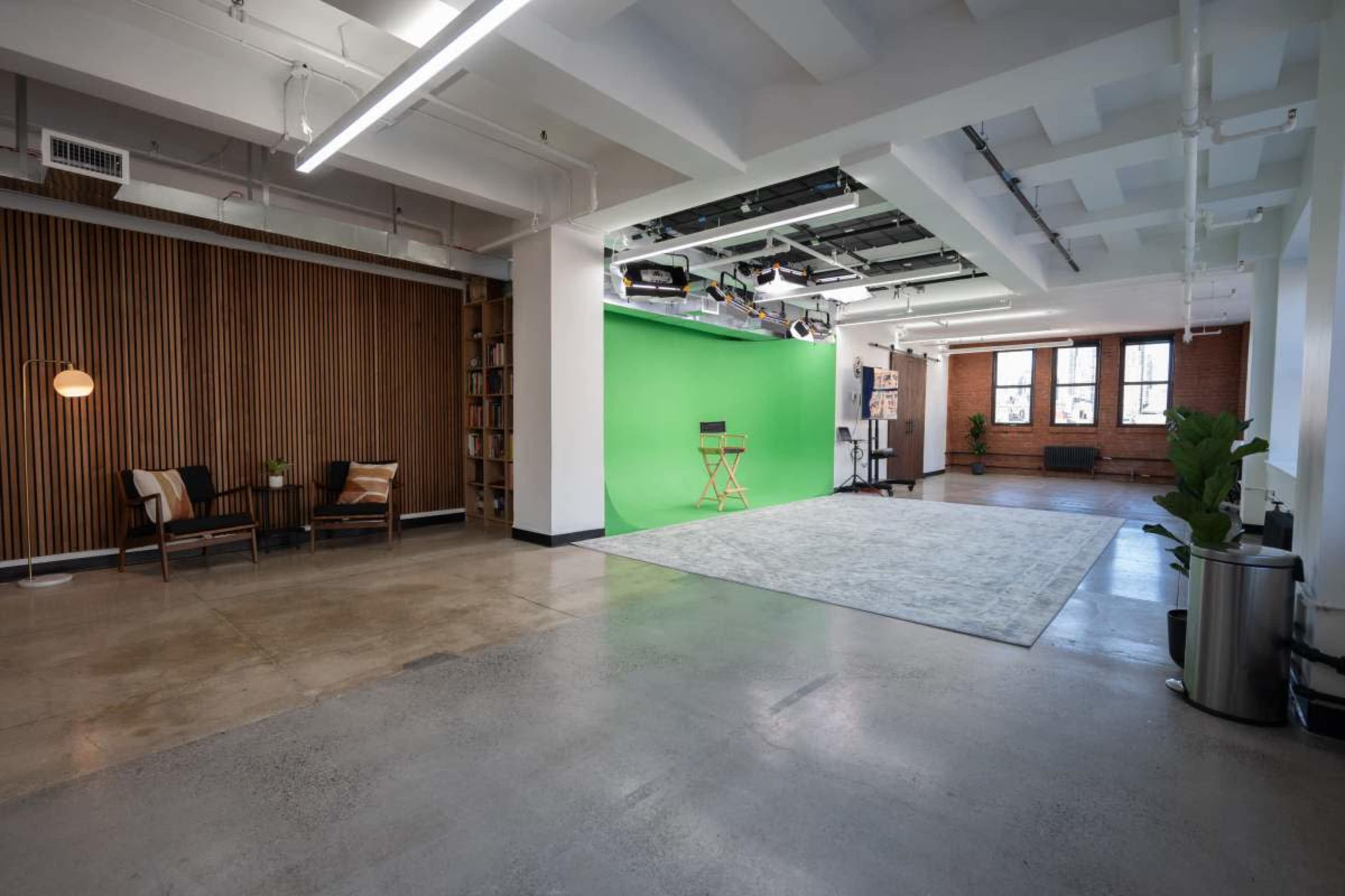 The image shows a modern, spacious studio with a green screen wall, wooden paneling, and a seating area with two chairs.