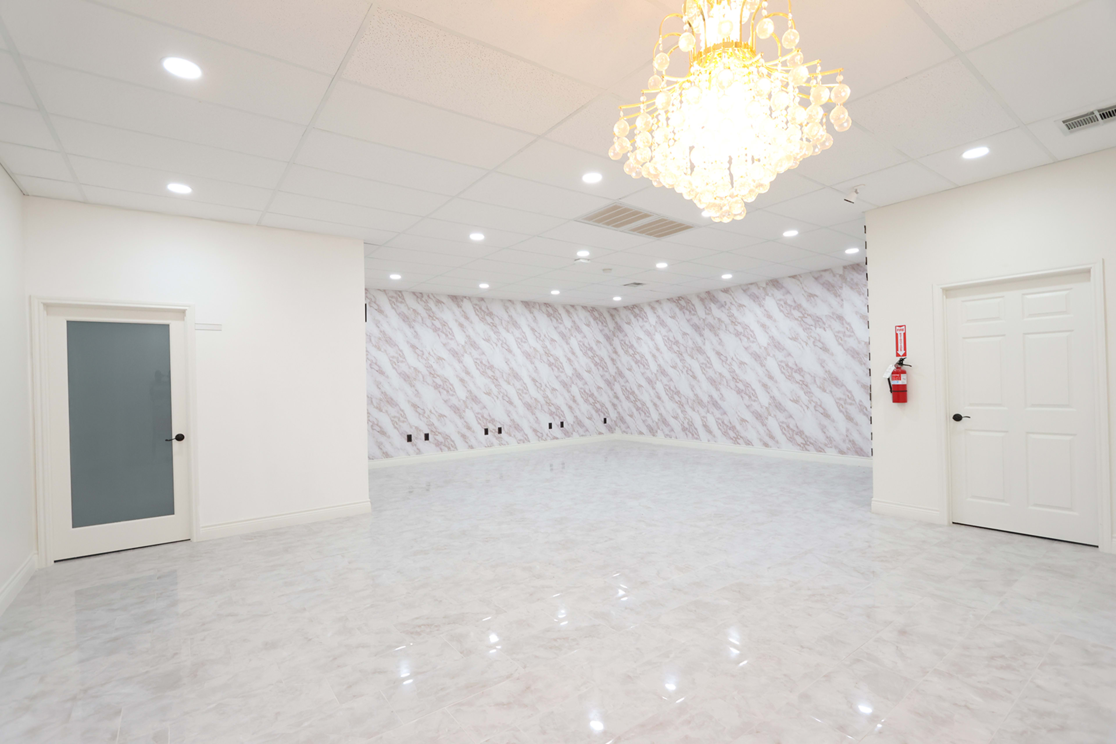 A spacious, well-lit room with marble floors, a patterned wall, and a chandelier hanging from the ceiling.