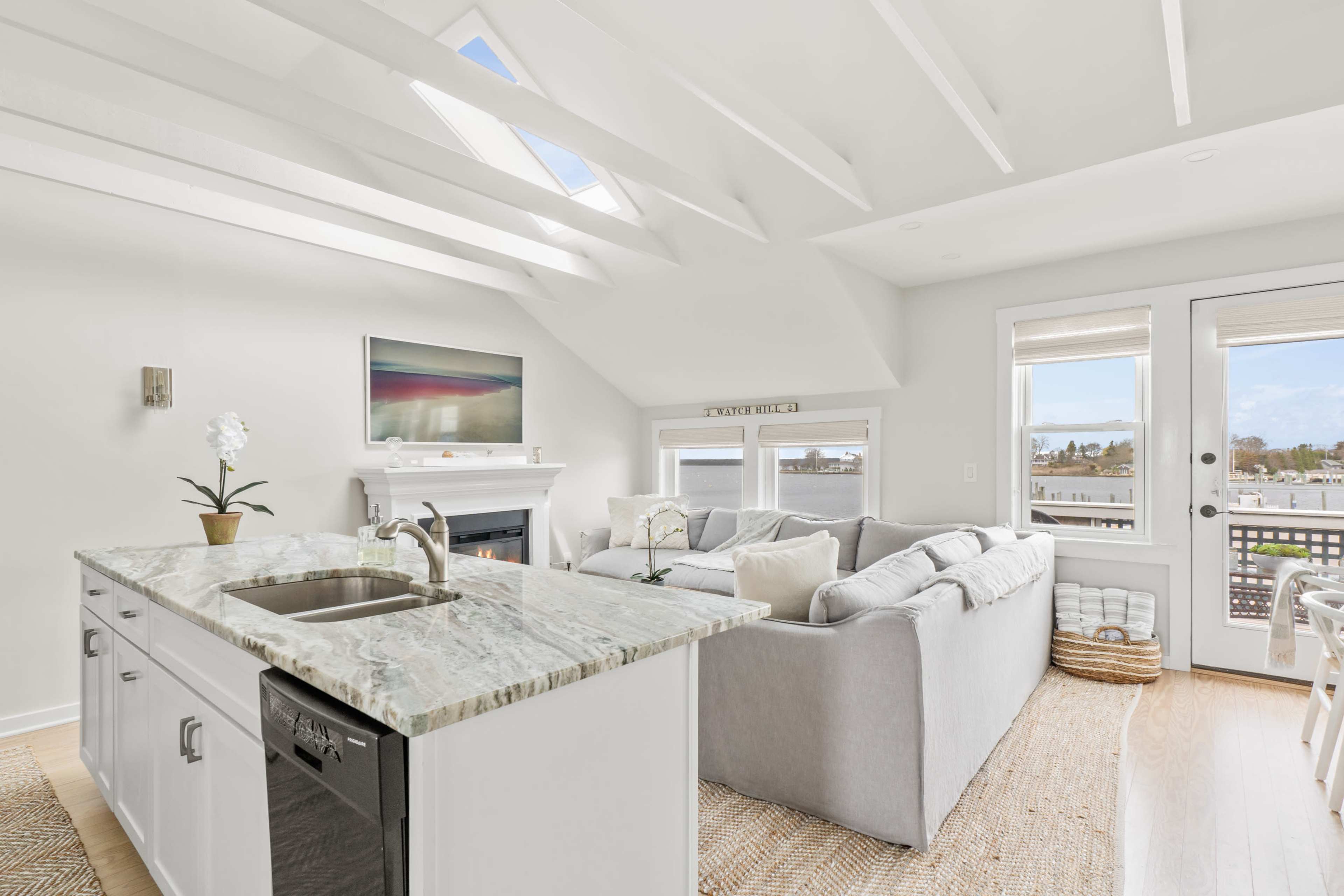 A bright living room with a fireplace, a large sectional sofa, and an open kitchen with a granite countertop.