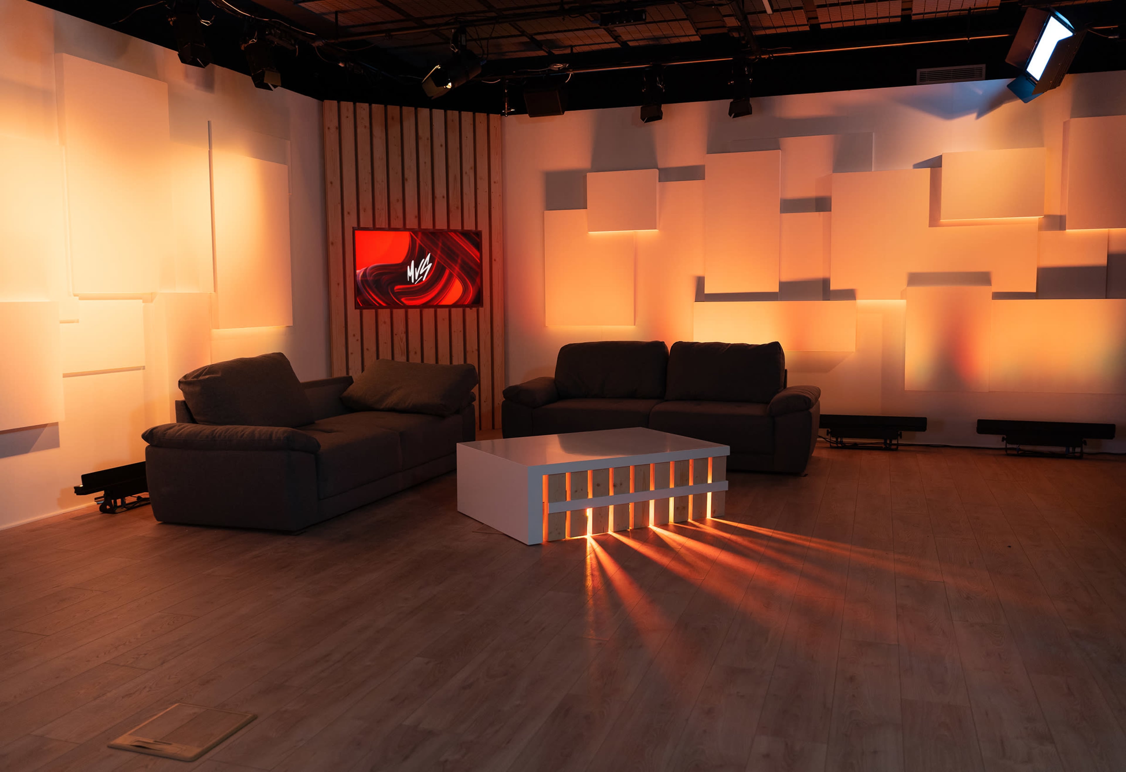 A modern studio space with two sofas and a white coffee table, illuminated by soft orange lighting.