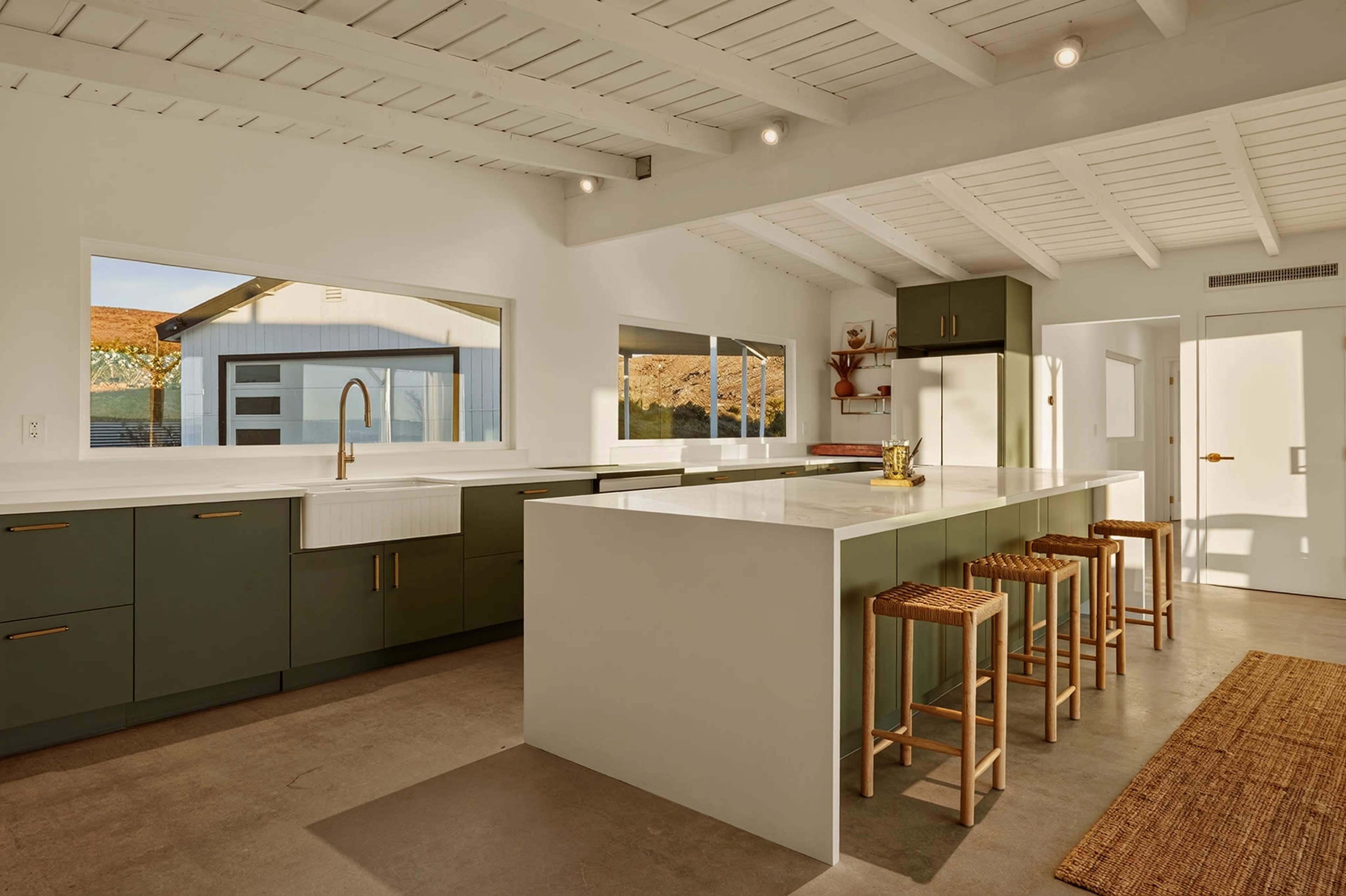 The kitchen features a modern design with green cabinetry, a large island, and natural light streaming in through large windows.