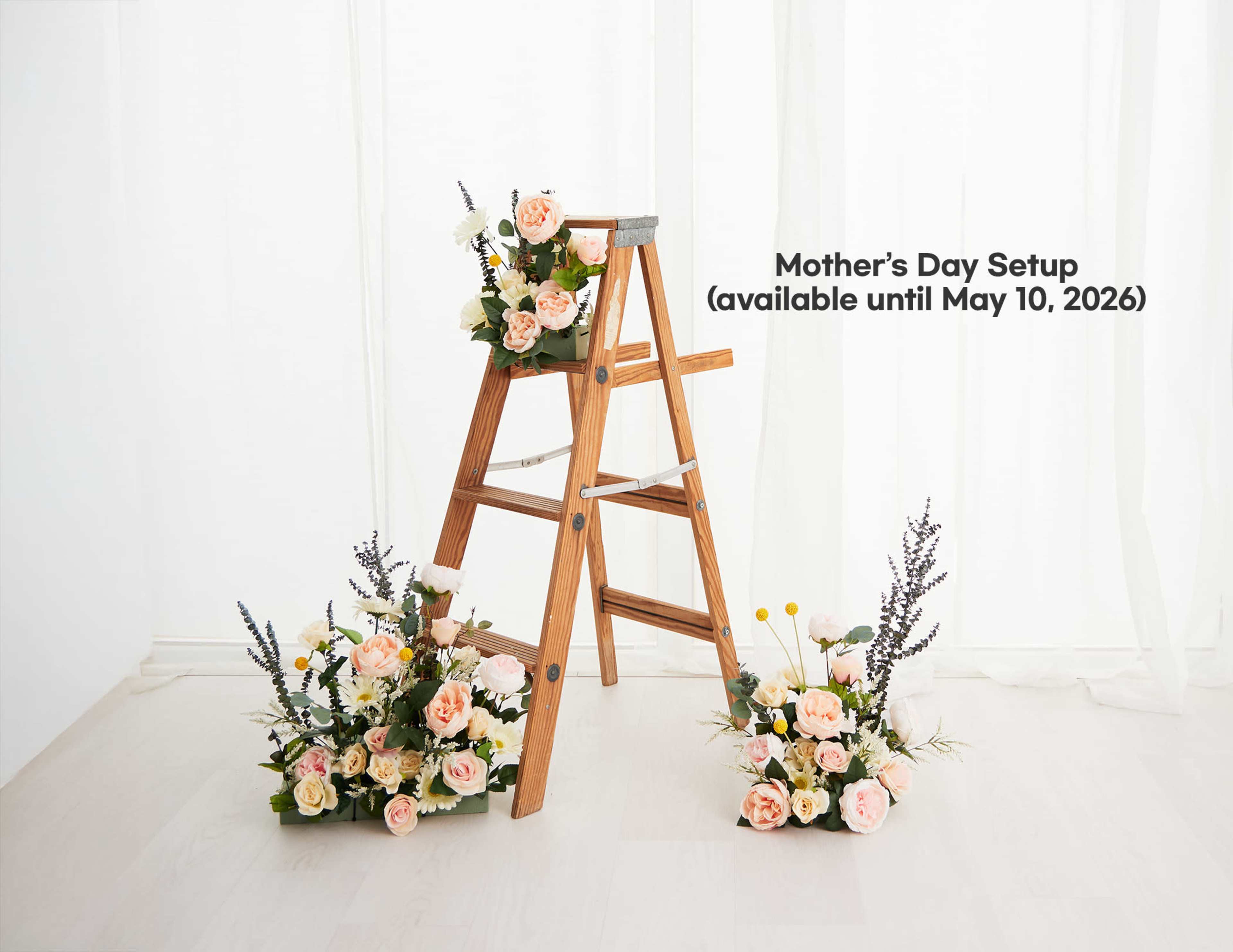 A wooden ladder displays floral arrangements with pink and white flowers, positioned alongside additional flower arrangements on the floor.