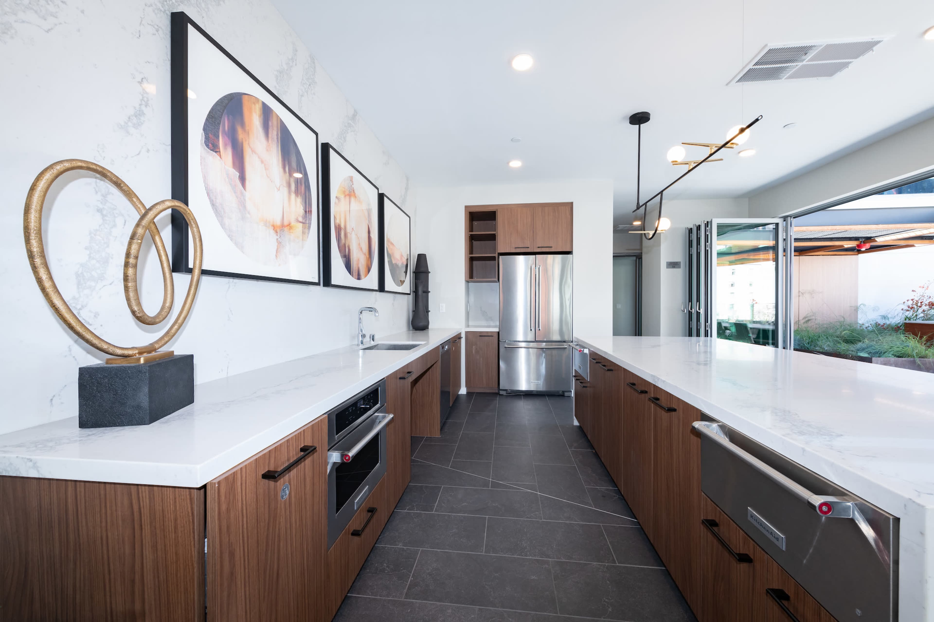 A modern kitchen features marble countertops, wooden cabinetry, and stainless steel appliances, with decorative art on the walls.
