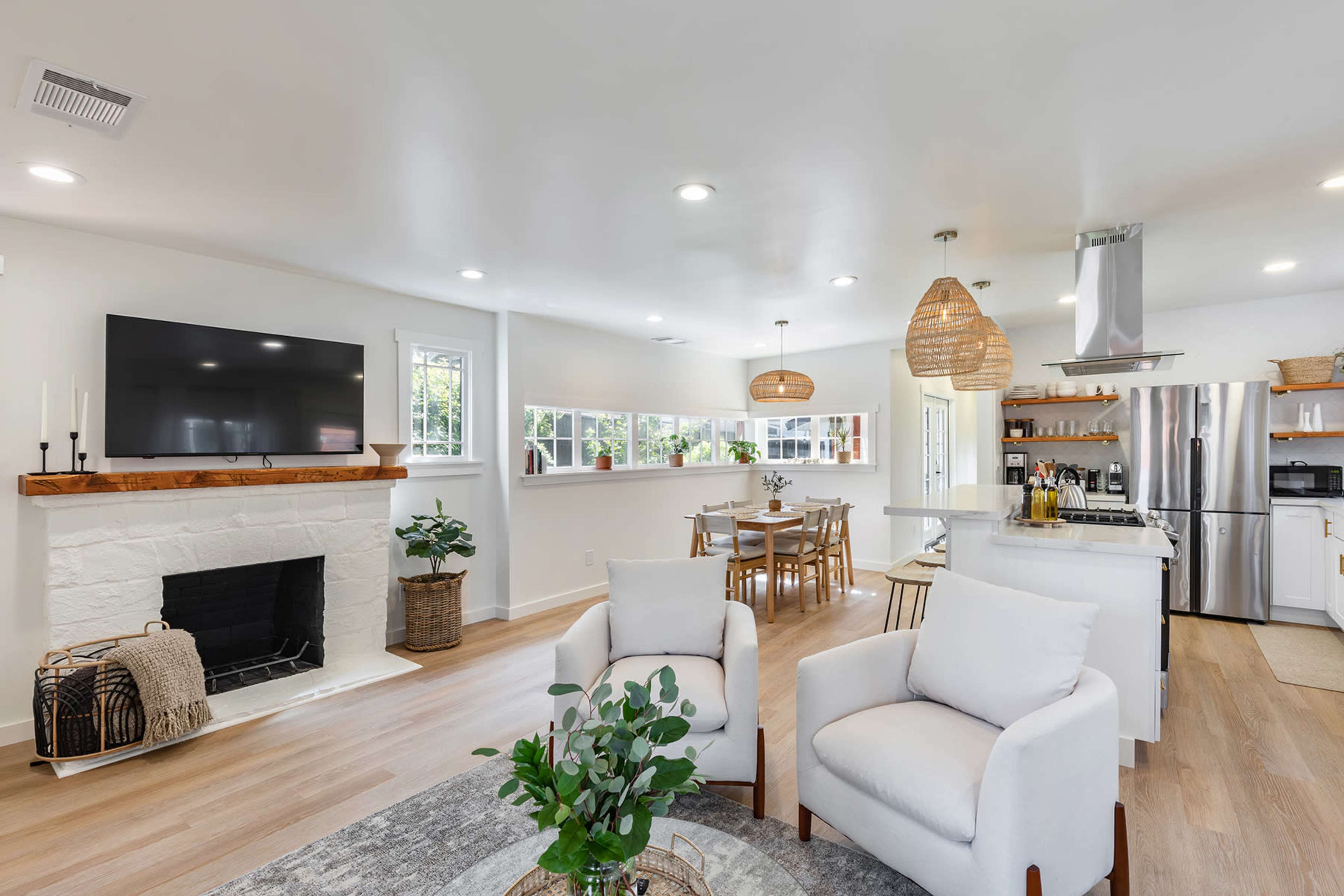 A modern living area features a fireplace, a wall-mounted TV, a dining table, and an open kitchen with island seating.
