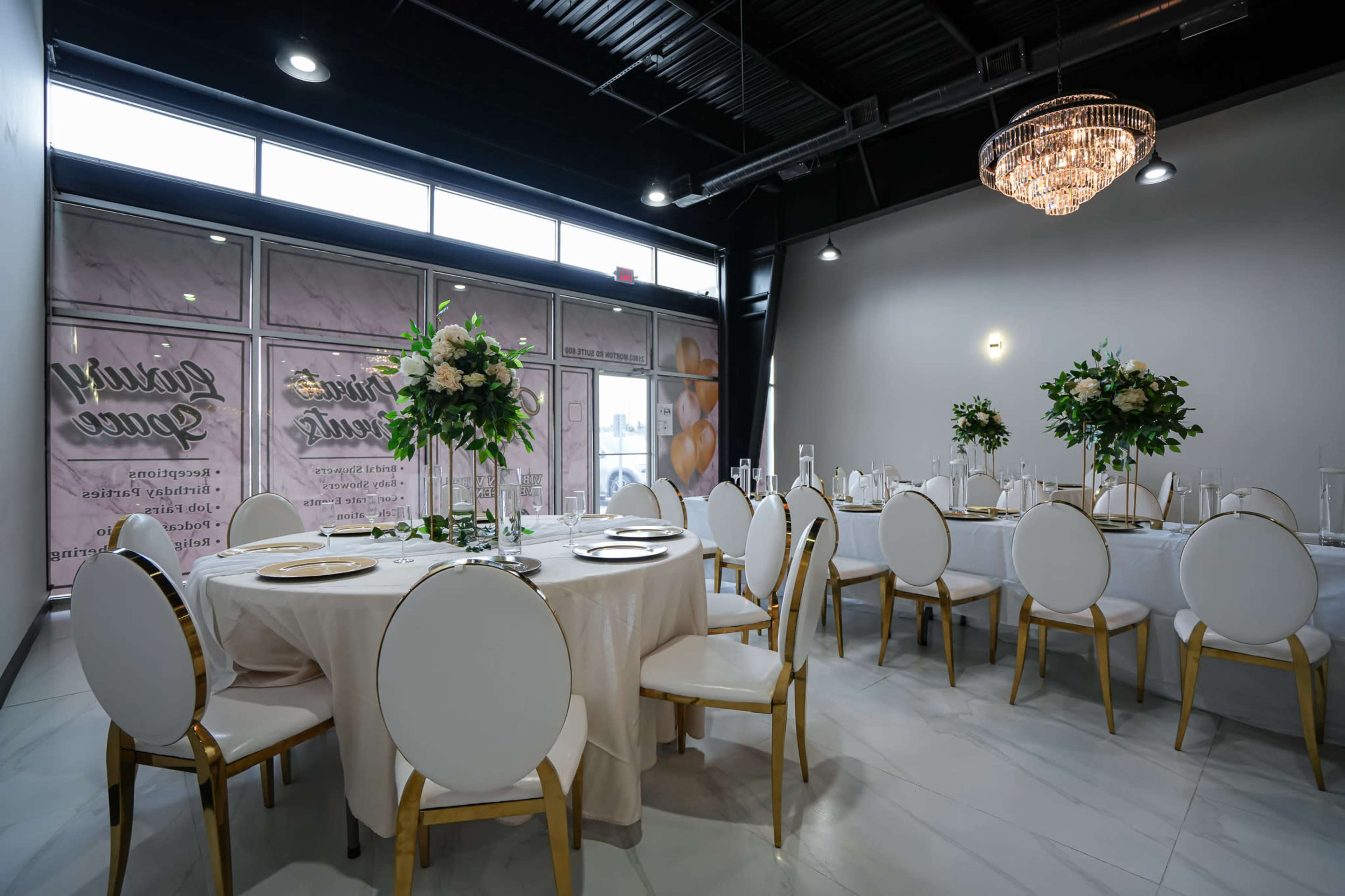 A formal dining room features round tables with white tablecloths and elegant chairs, adorned with floral centerpieces and a chandelier overhead.