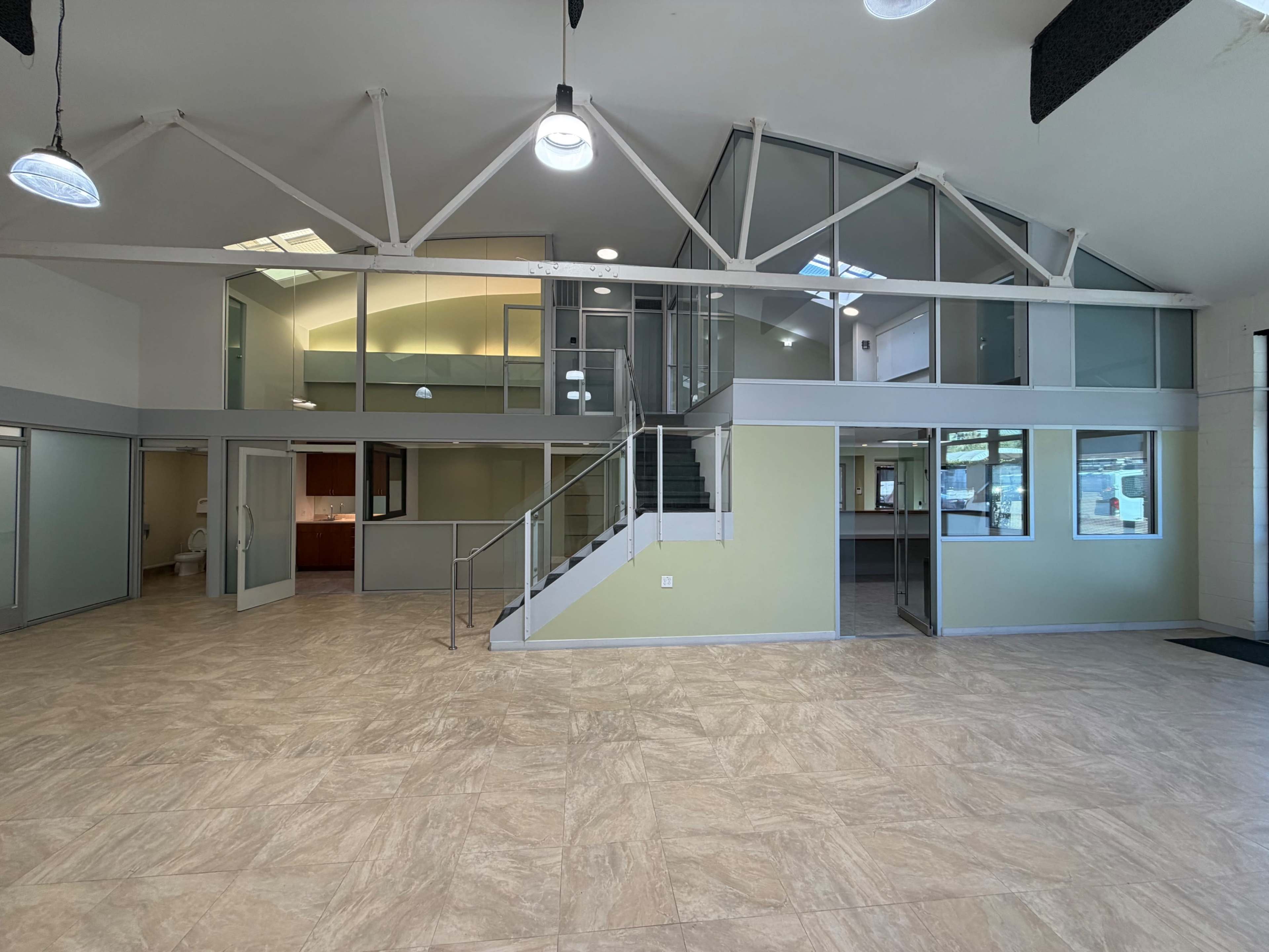 The image shows a spacious, modern interior of an office building featuring large windows, a staircase, and separated rooms.