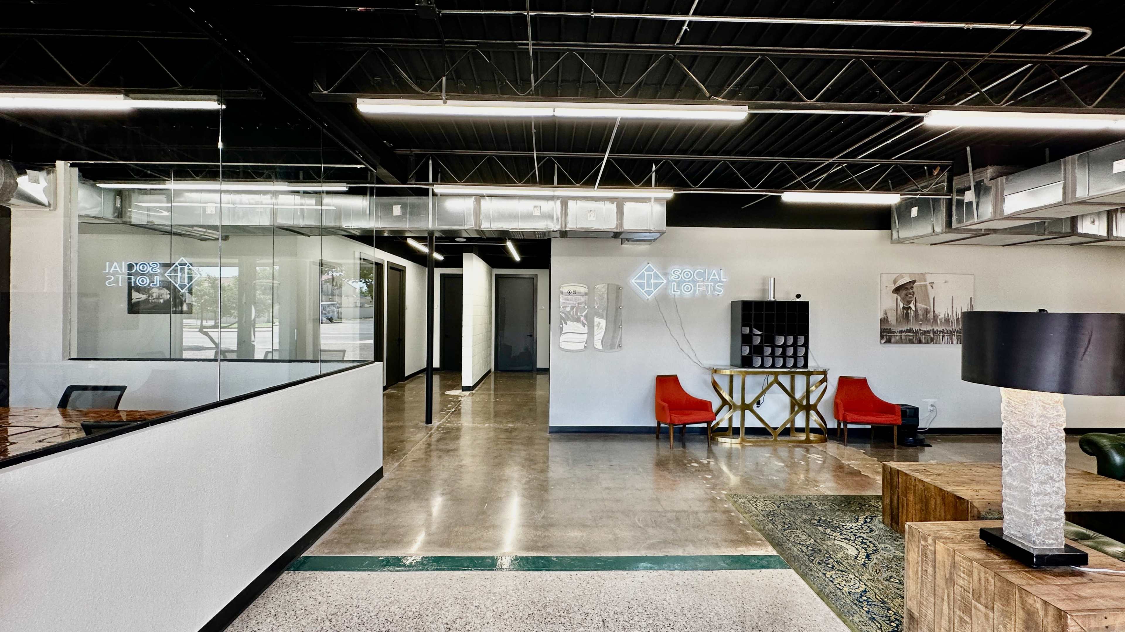 The image shows a modern office interior with a reception area featuring red chairs, a decorative table, and glass partitions.