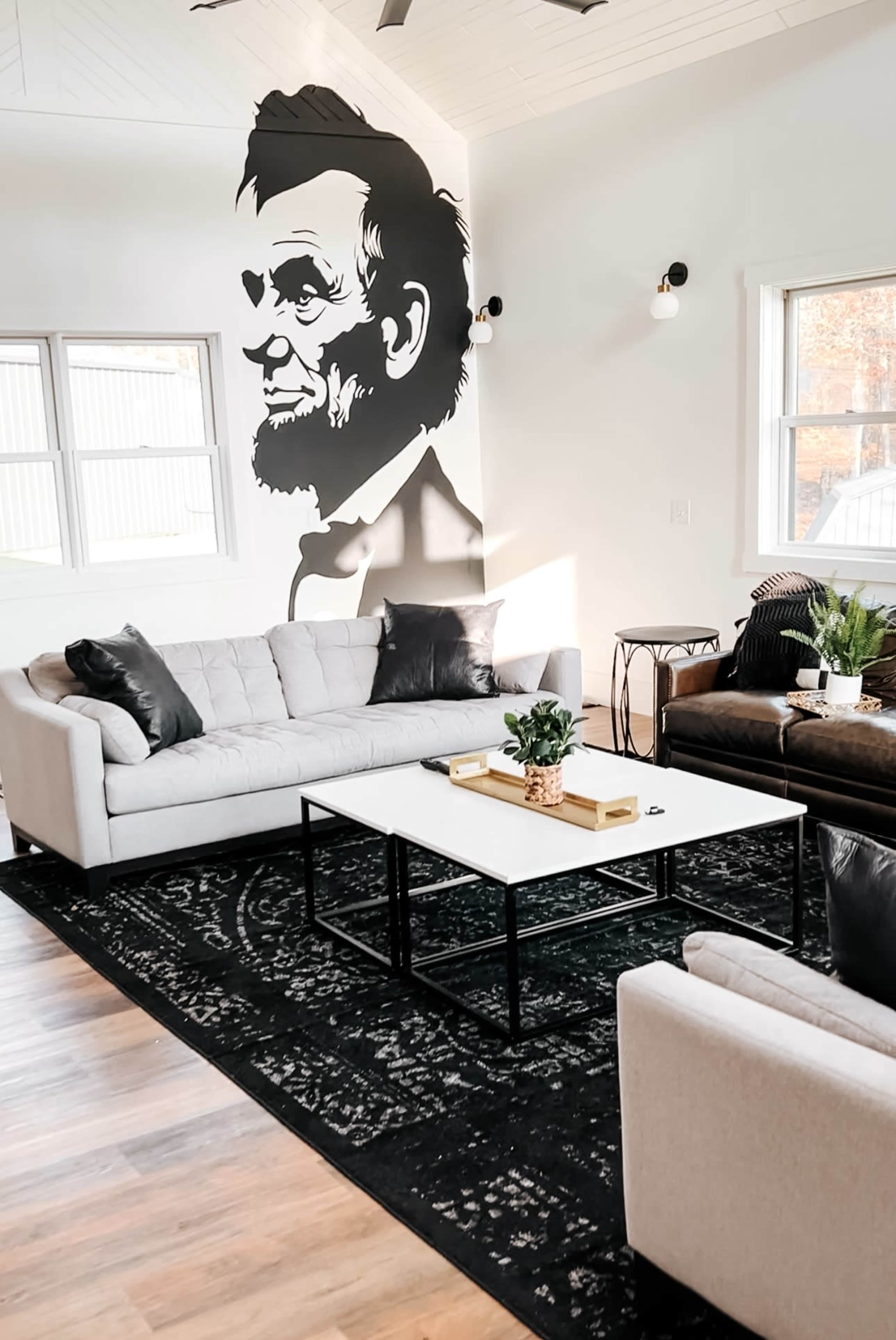 The living area features a mural of Abraham Lincoln on a white wall, with two sofas and a coffee table on a dark patterned rug.