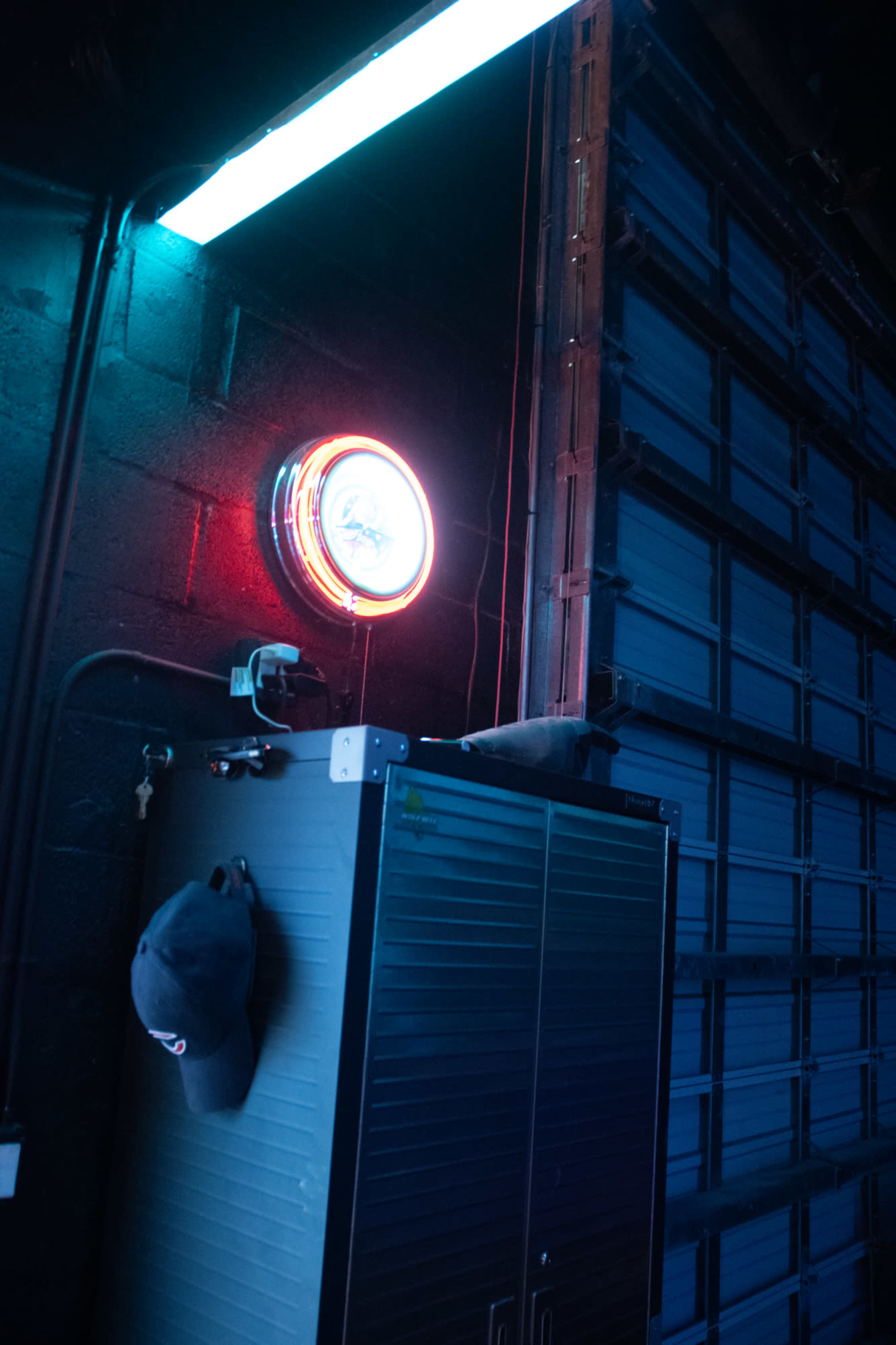 The image shows a dark garage with a storage cabinet, a neon clock, and a blue light fixture along the wall.