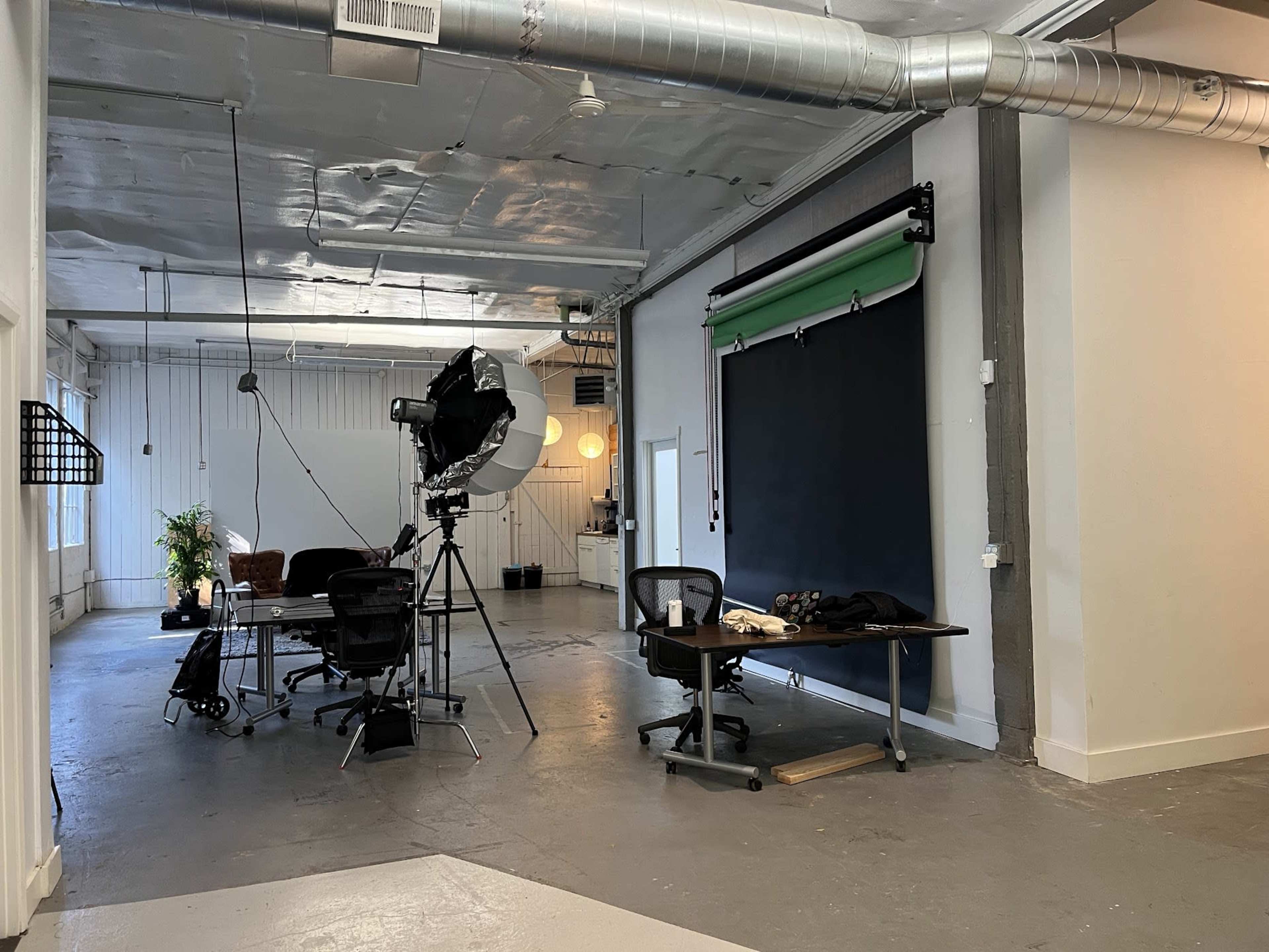 A large, well-lit studio space with a black backdrop, photography equipment, a desk, and a chair.