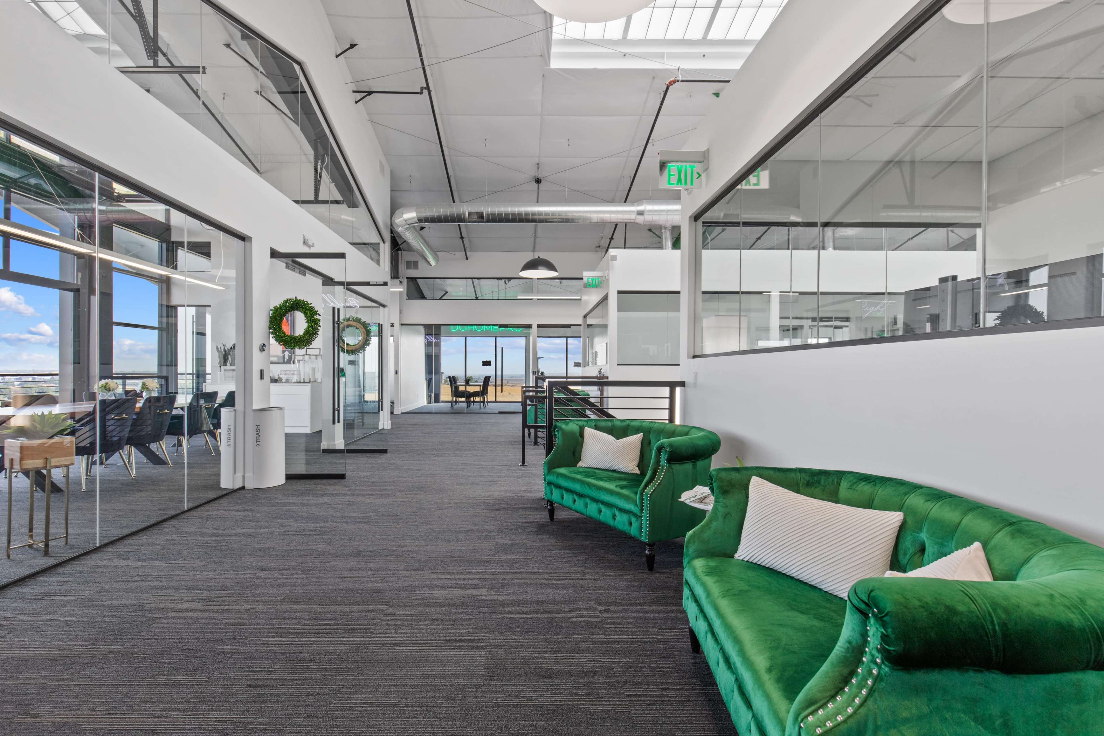 The image shows a modern office corridor with green velvet sofas on one side and glass-walled meeting rooms on the other.