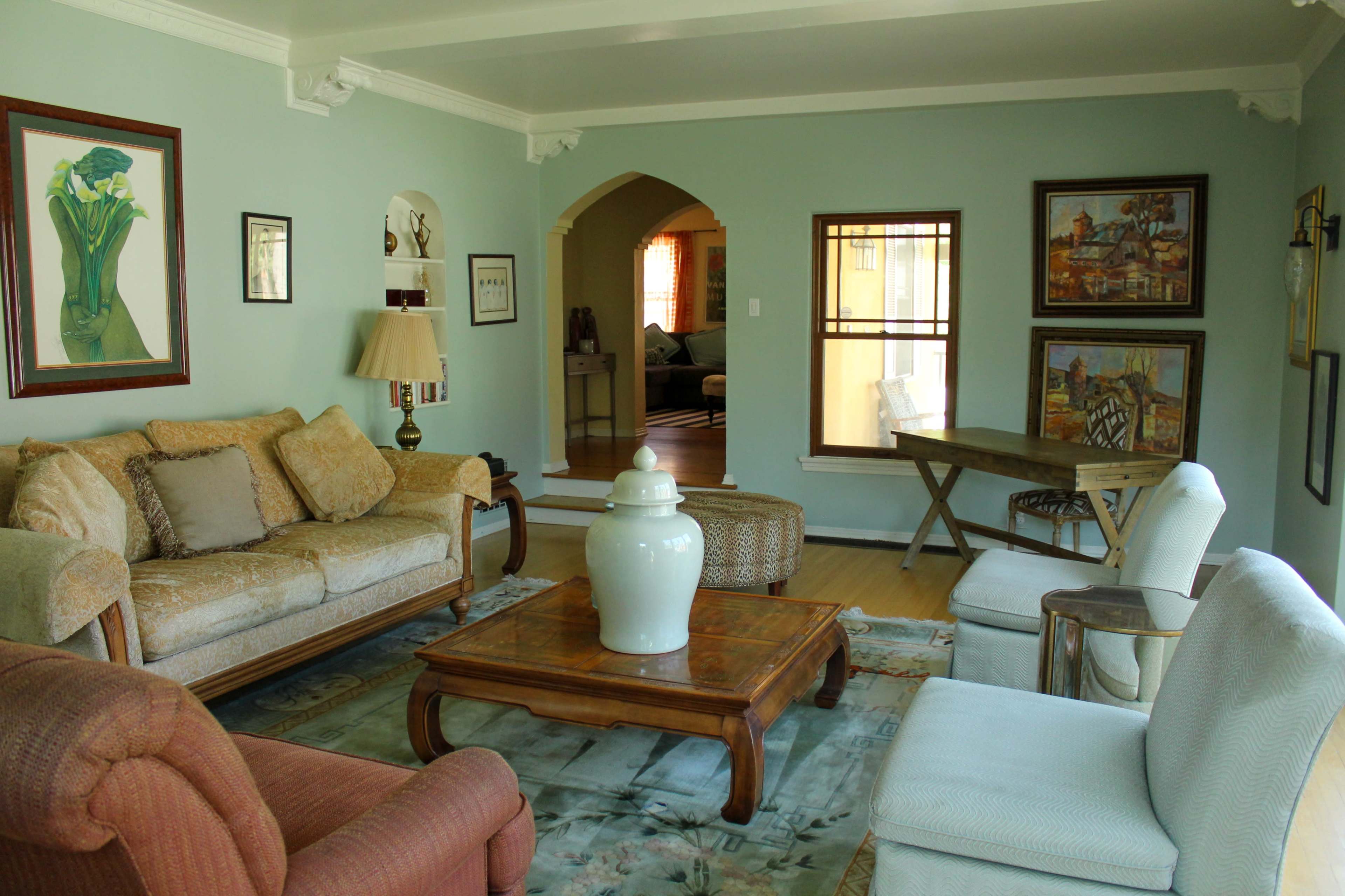 The image shows a spacious living room featuring light blue walls, a variety of seating options, a wooden coffee table, and decorative artwork on the walls.