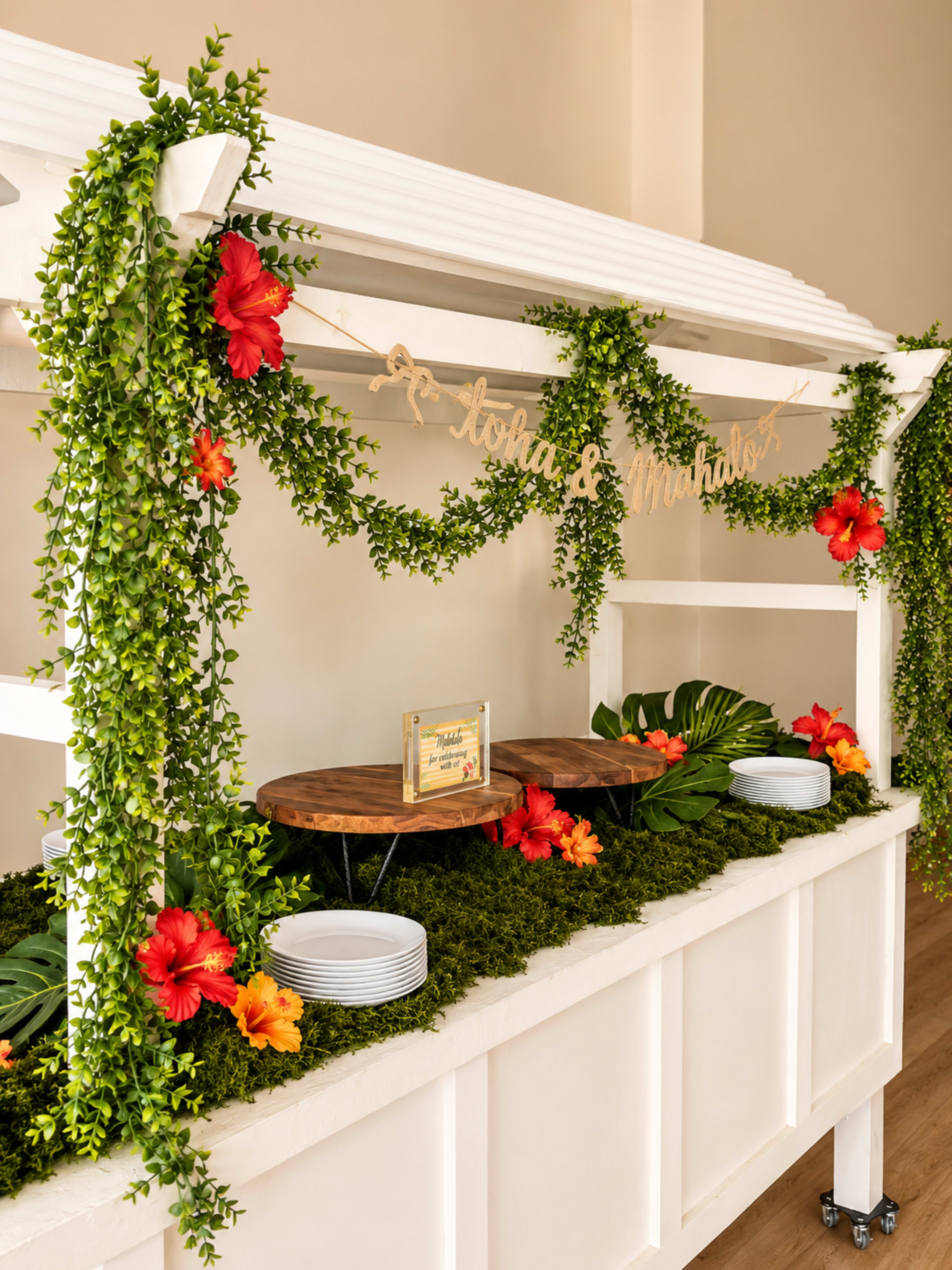 A decorated food serving station features greenery, vibrant flowers, and plates arranged neatly on a white structure.