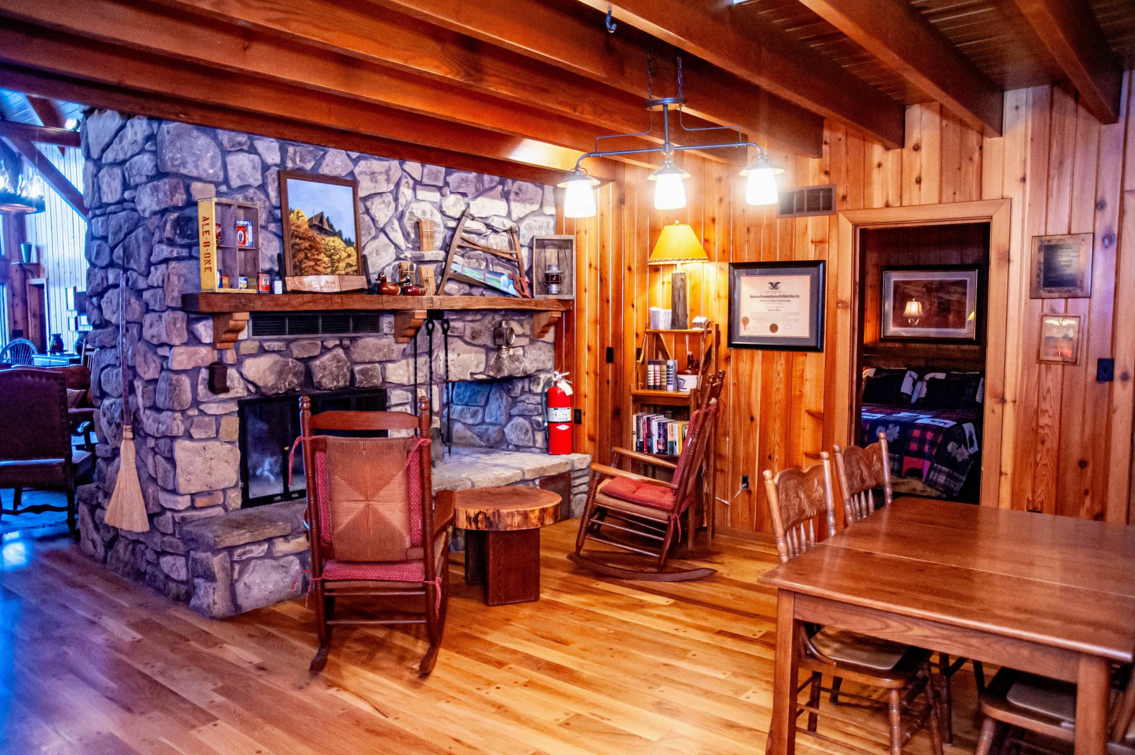 A cozy wooden interior with a stone fireplace, a wooden dining table, and several chairs arranged around a rustic decor.