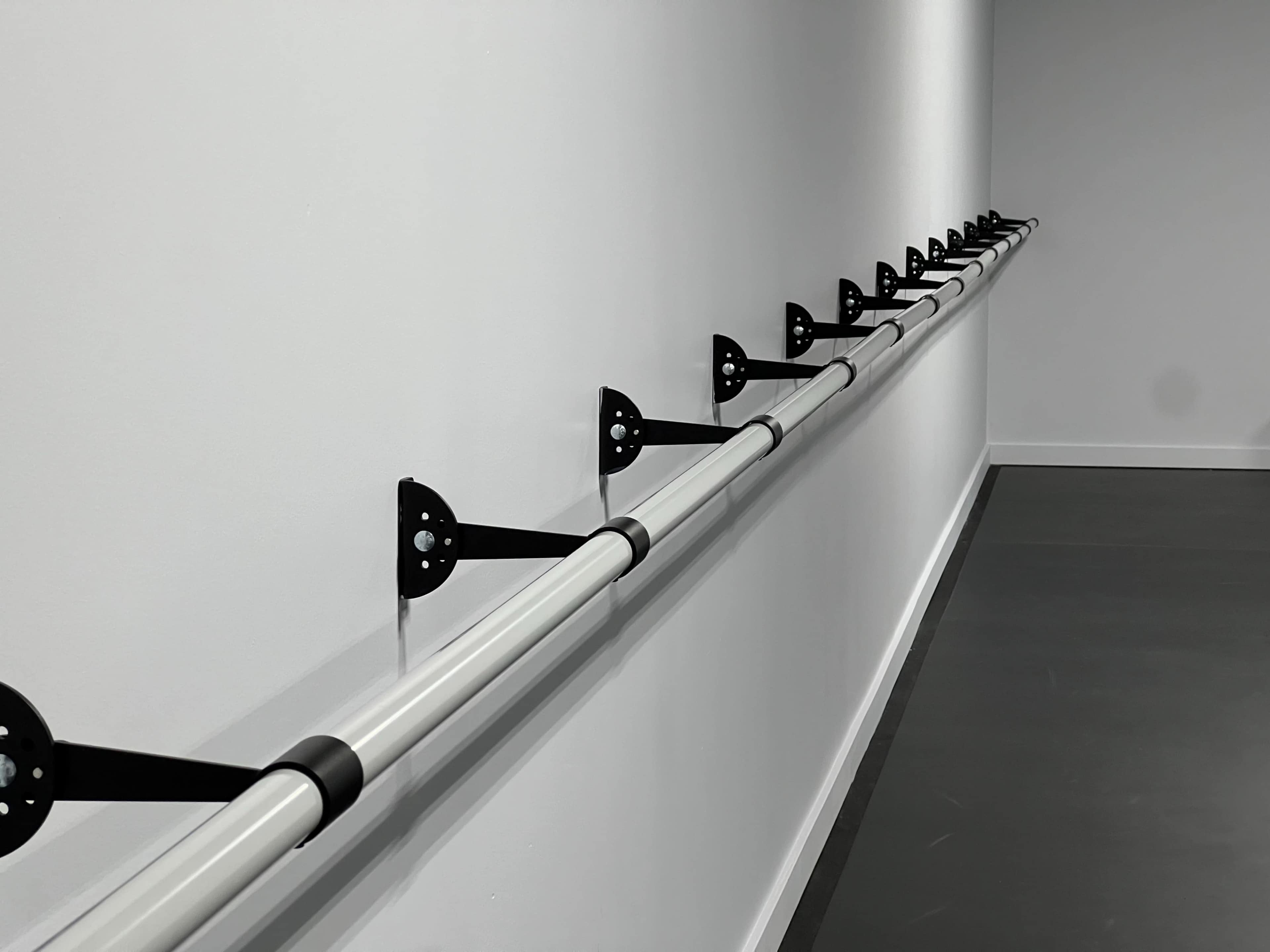 A row of black mounting brackets is attached to a white wall, supporting a long, horizontal white handrail.