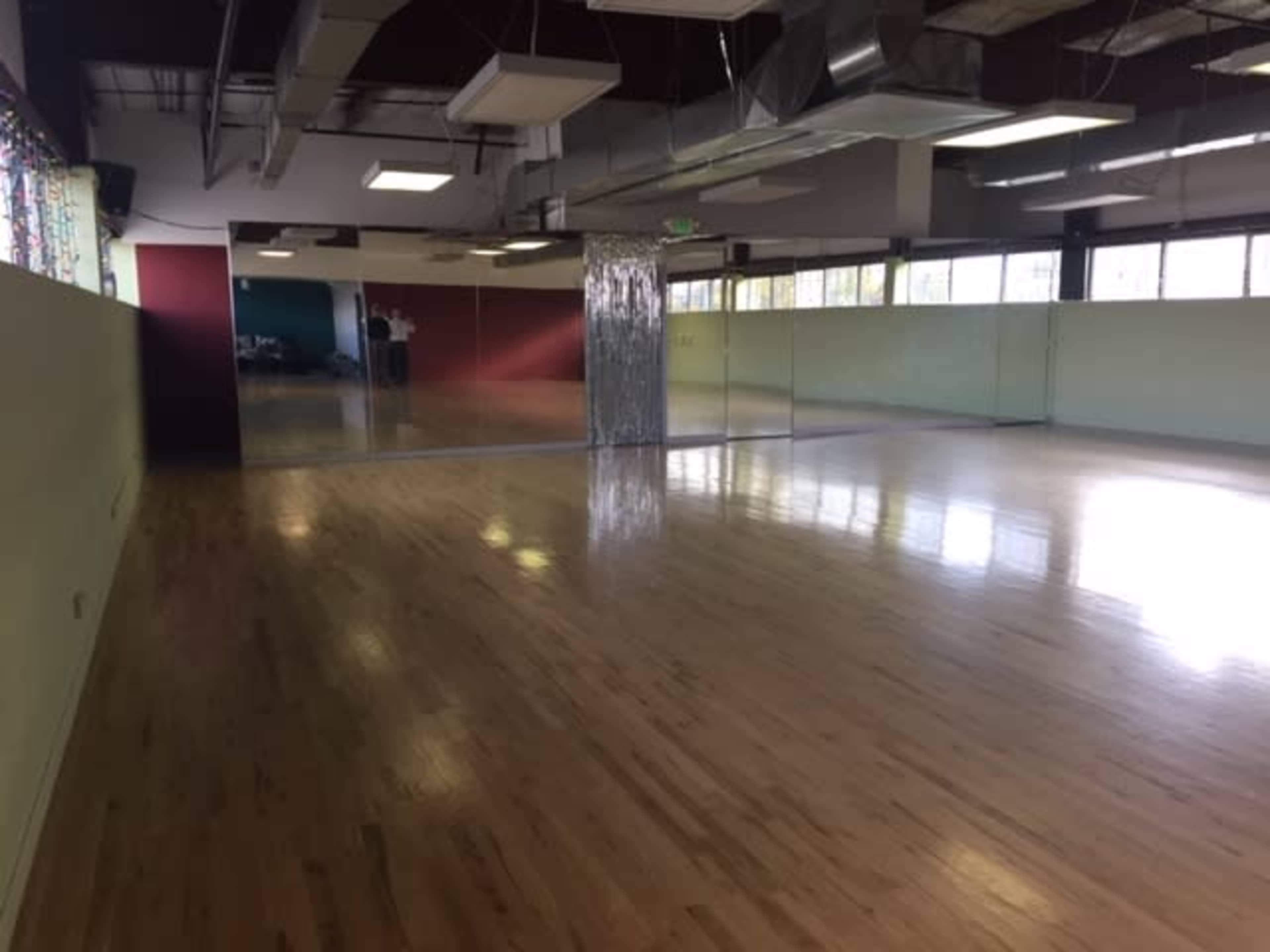 An empty, well-lit dance studio with hardwood floors and large mirrors on one wall.