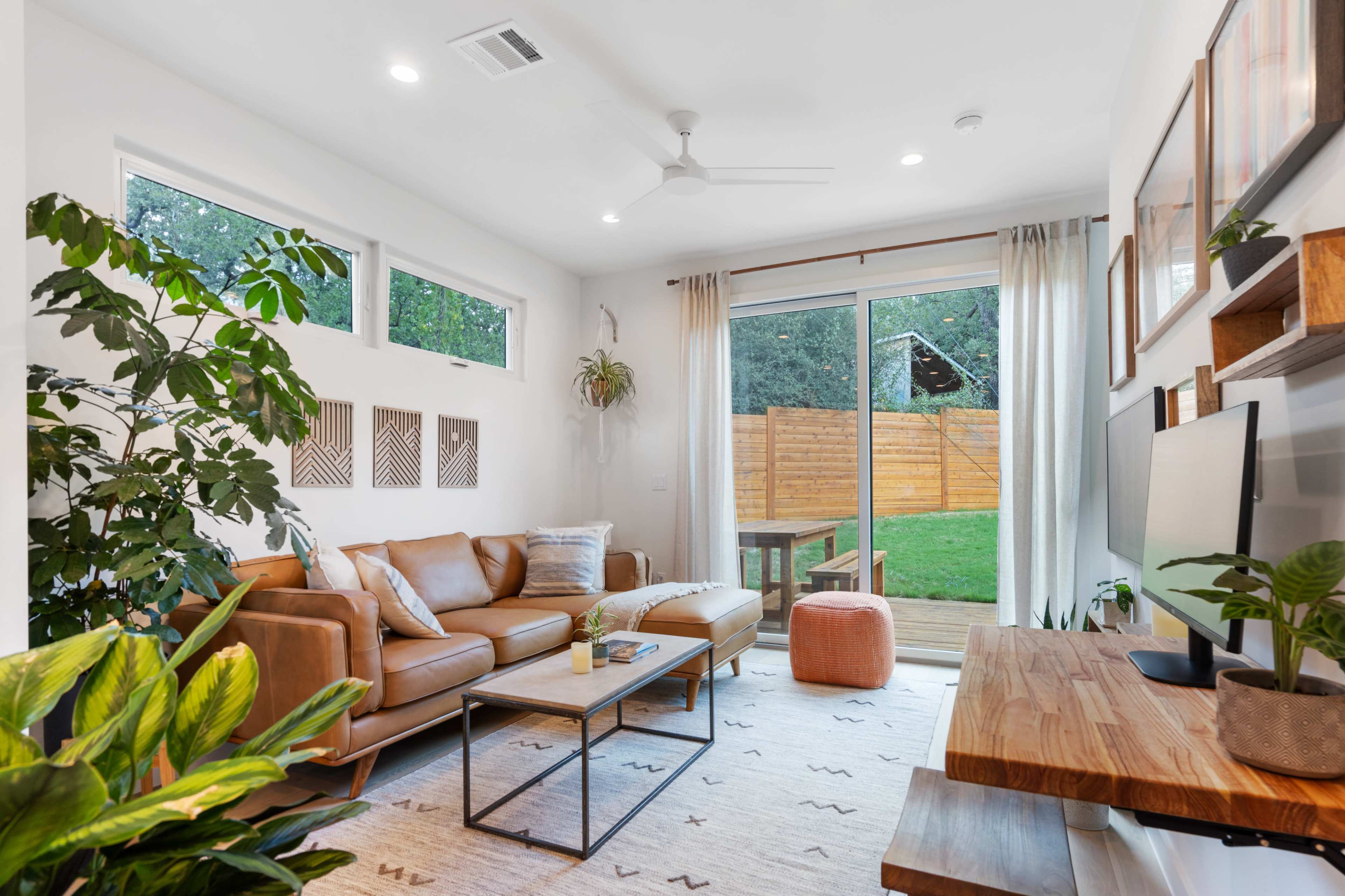 A modern living room features a brown leather sofa, a coffee table, and a large sliding glass door leading to a backyard.