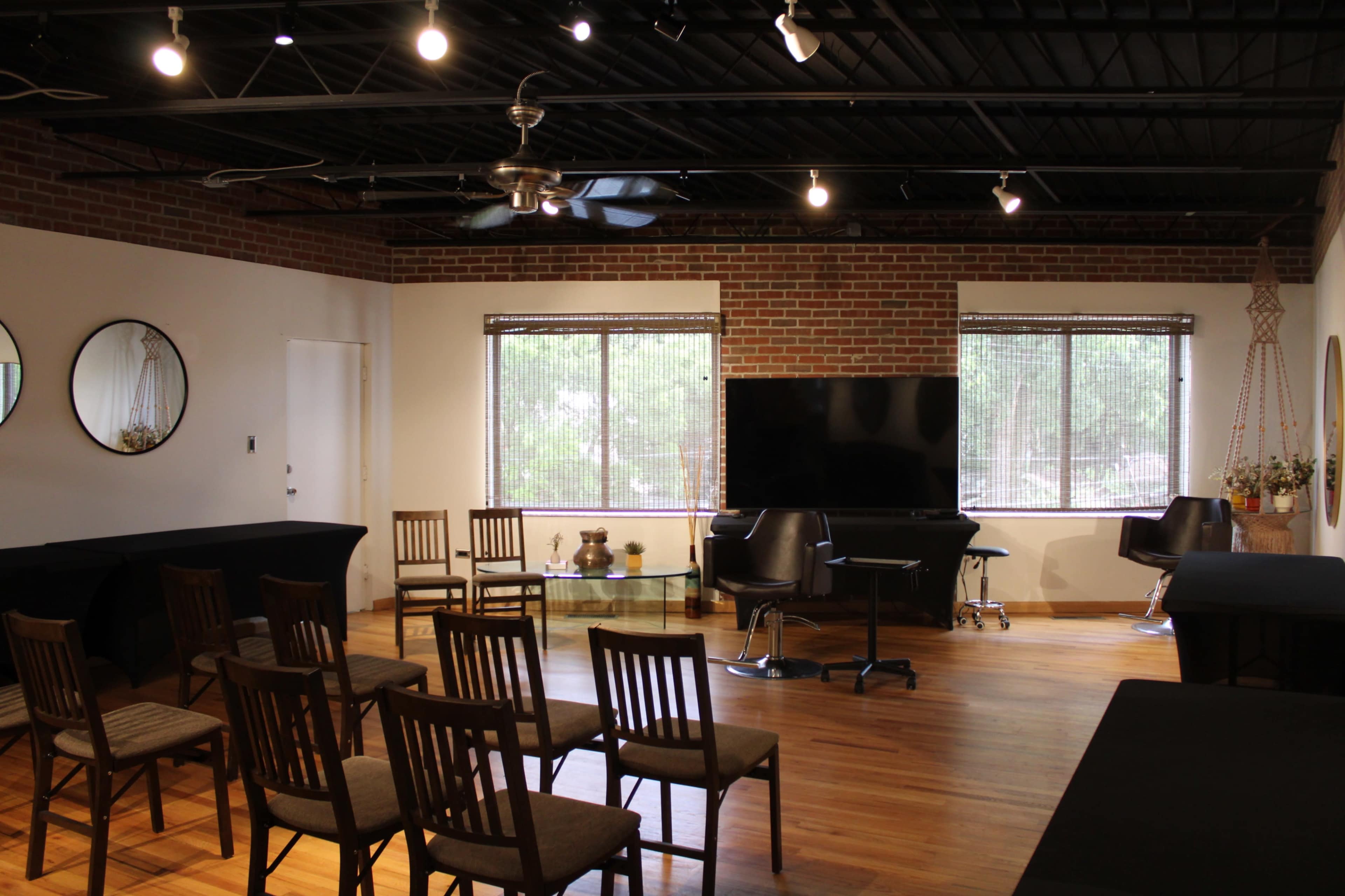 A meeting room features wooden chairs arranged facing a television, with large windows allowing natural light to enter.