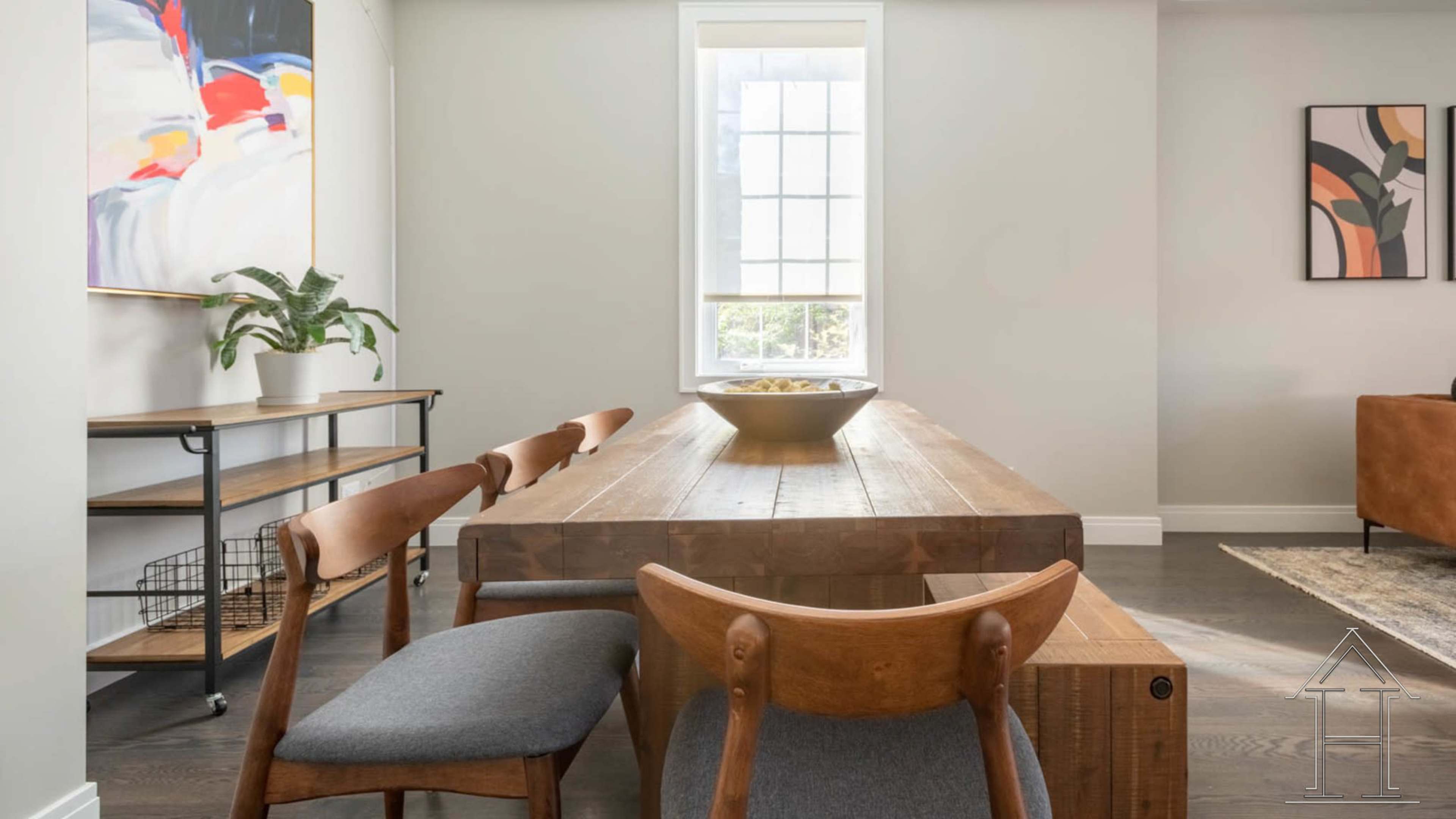 A dining area with a wooden table, several chairs, and a large window allowing natural light to enter.
