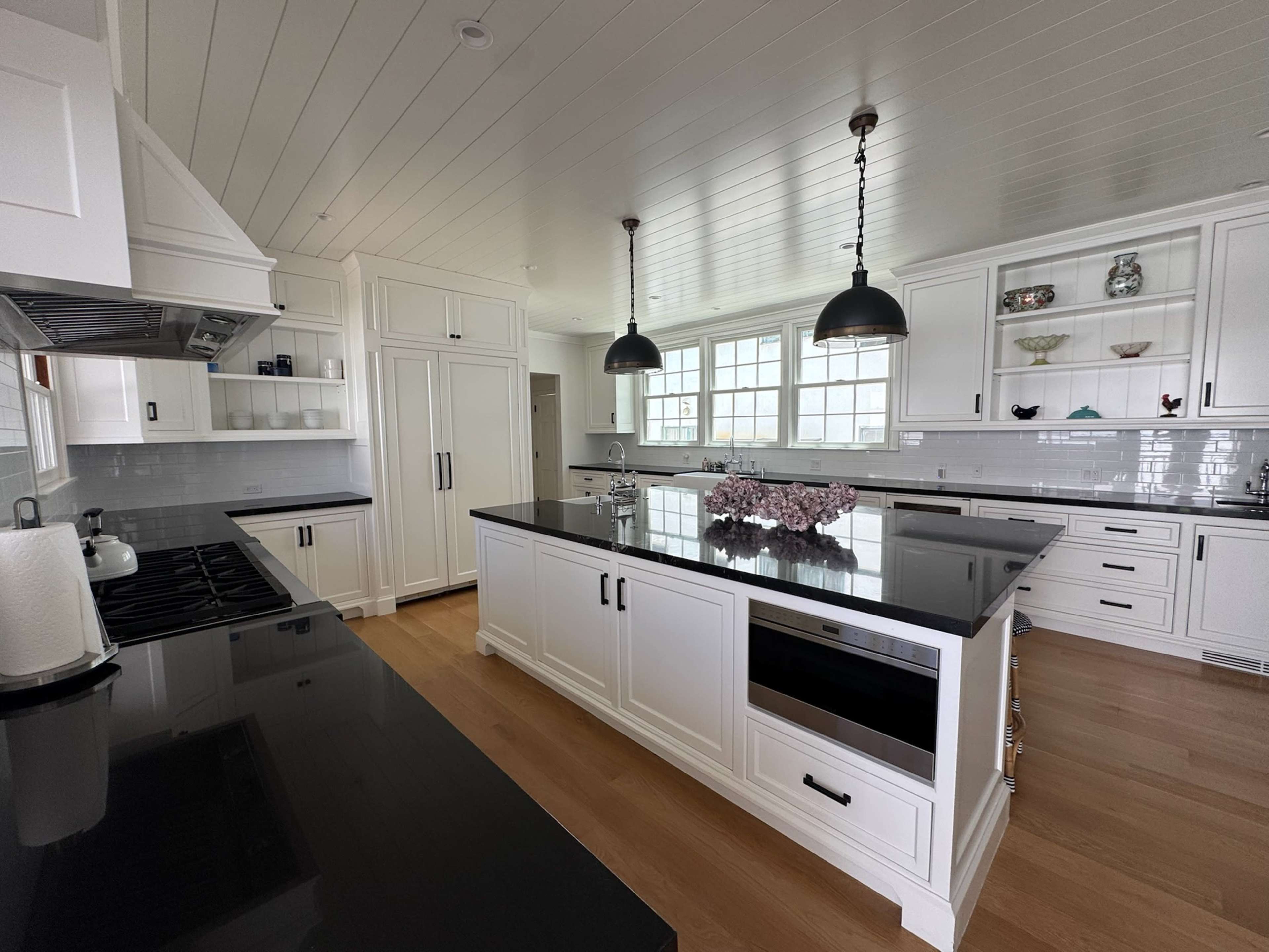 A spacious kitchen features white cabinetry, a large black countertop, and pendant lighting, with a row of windows allowing natural light.
