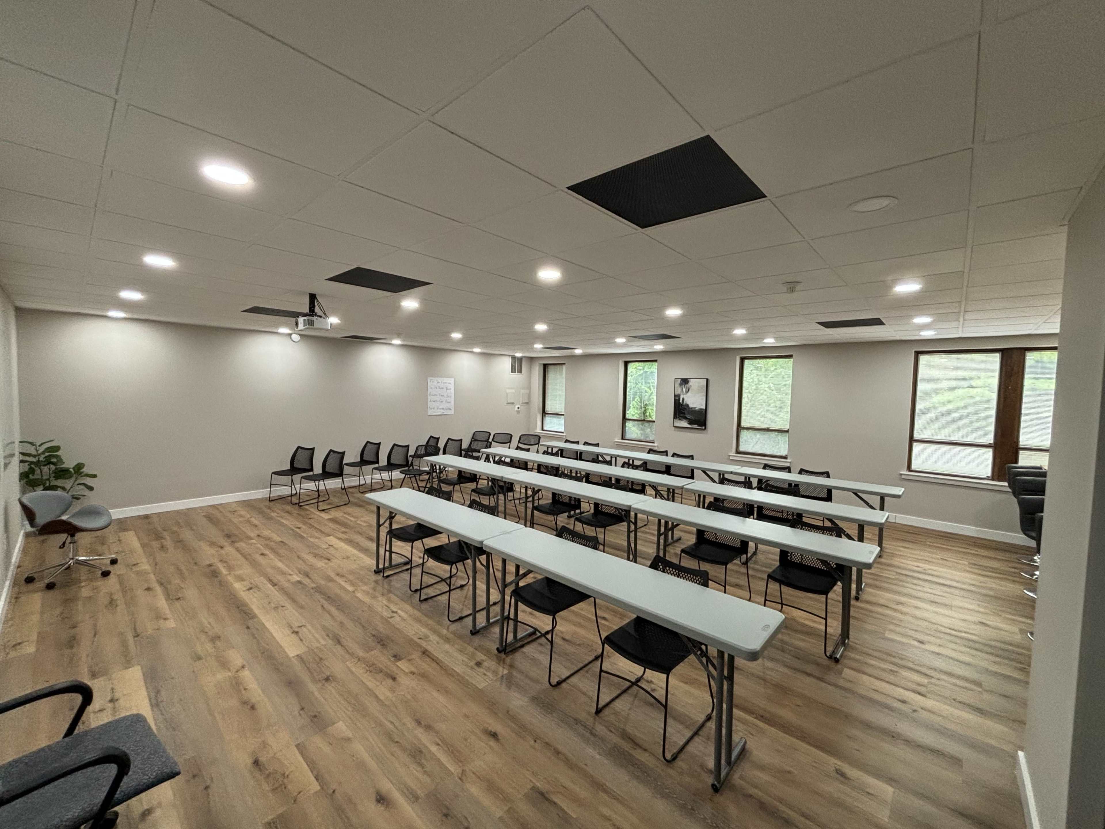 A modern conference room features rows of tables and chairs, large windows, and a wooden floor.