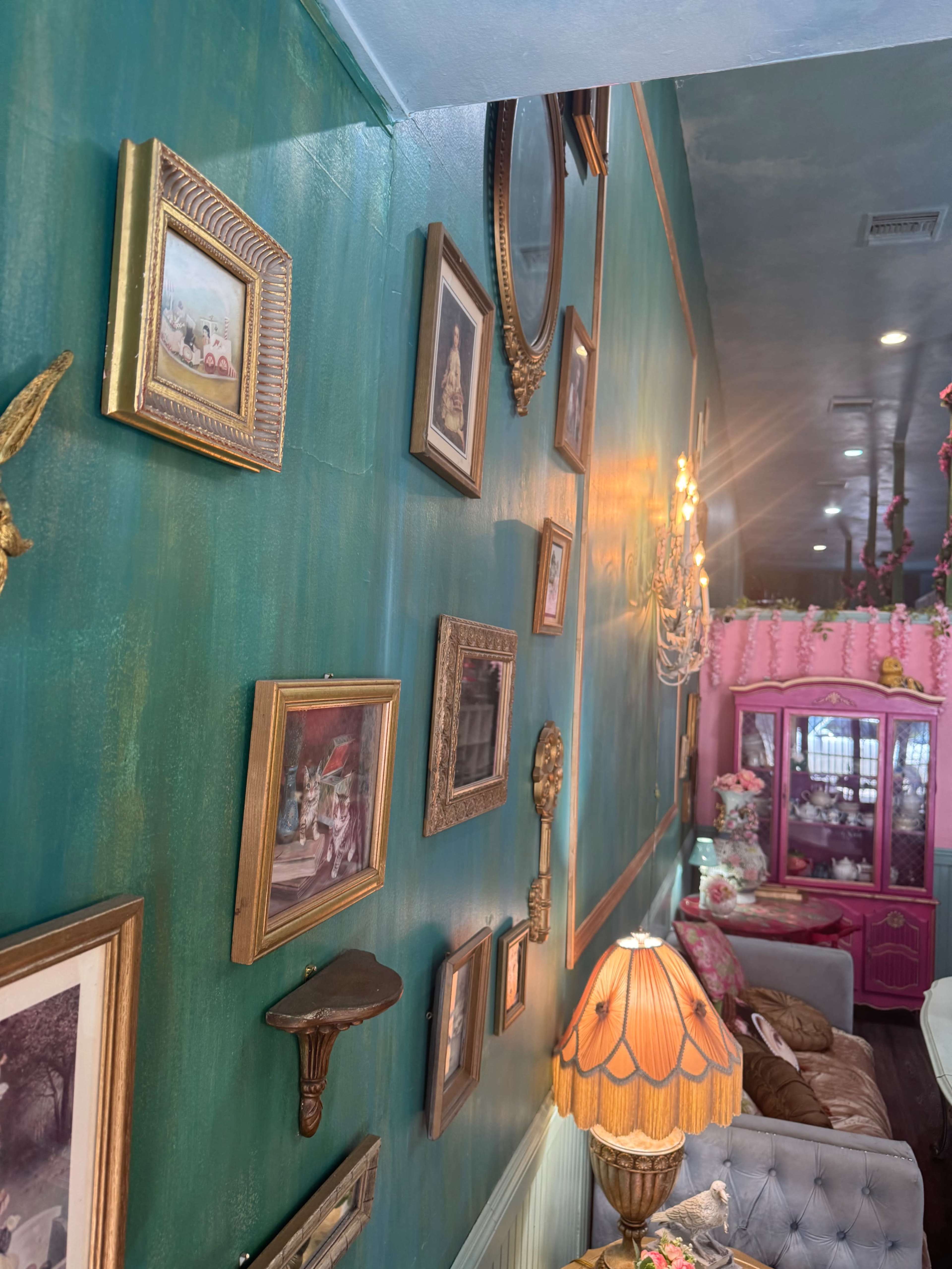 The image shows a colorful interior with a green wall adorned with various vintage picture frames and a decorative lamp in the foreground.