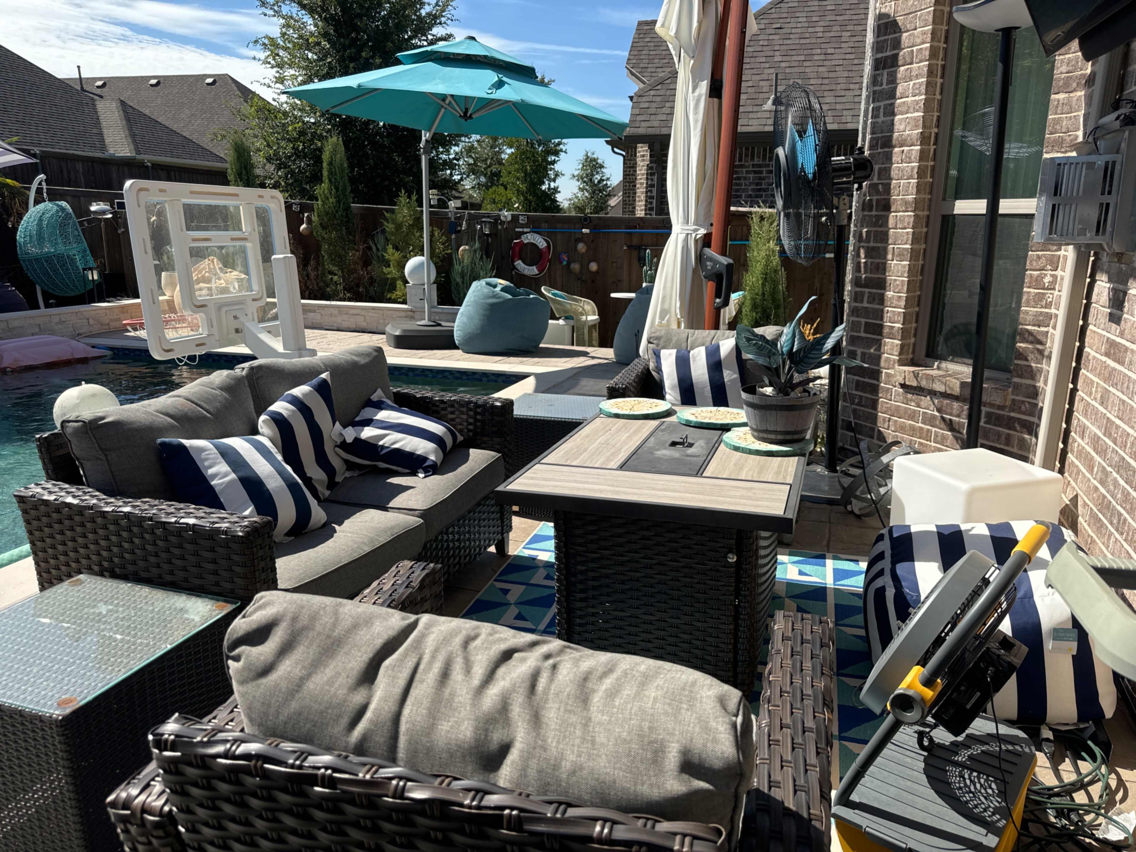 The image shows an outdoor seating area with striped cushions, a table, and an umbrella near a pool in a backyard setting.