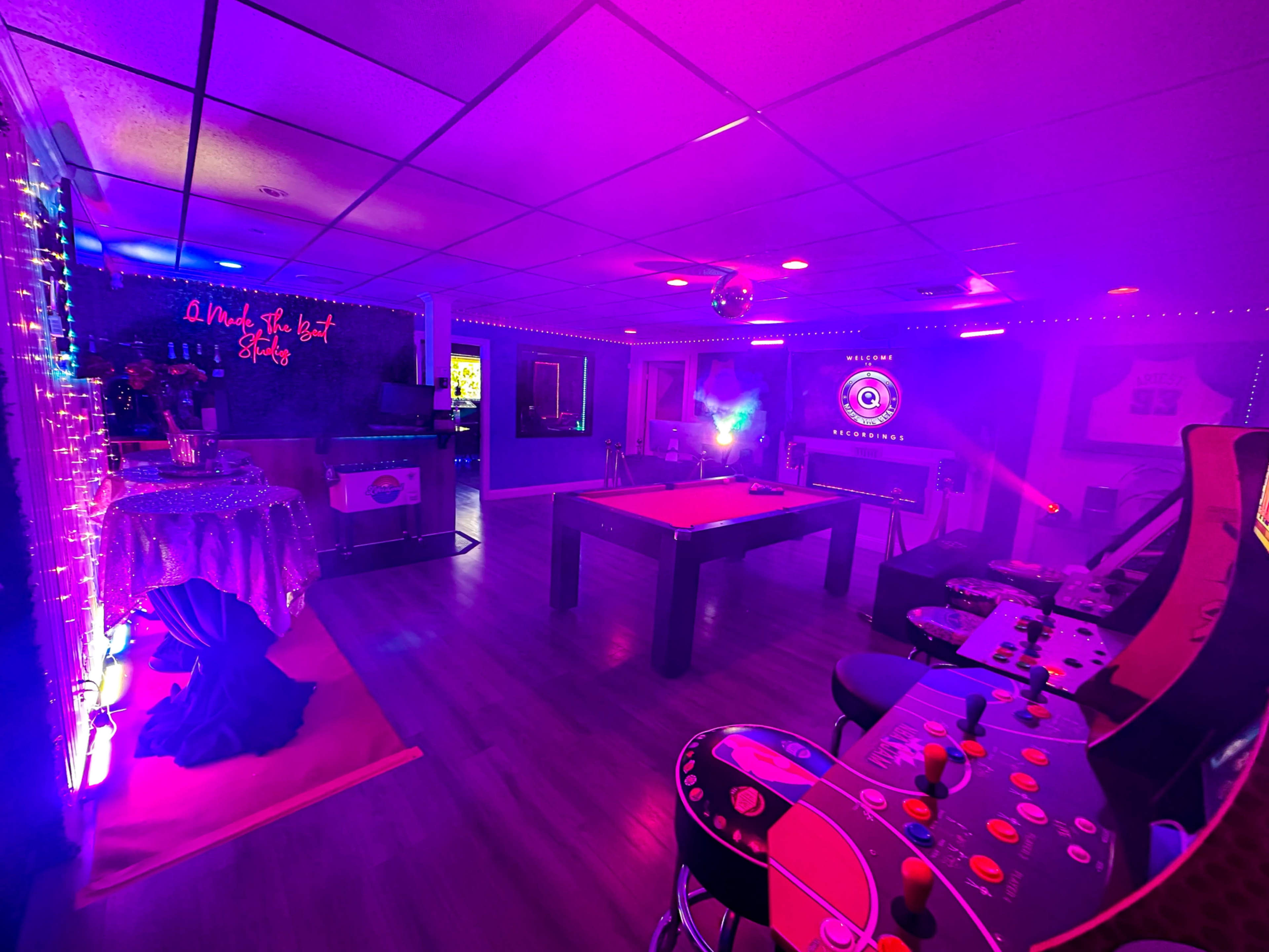 The image shows a dimly lit game room featuring a pool table, arcade machine, bar area, and various colorful lights.
