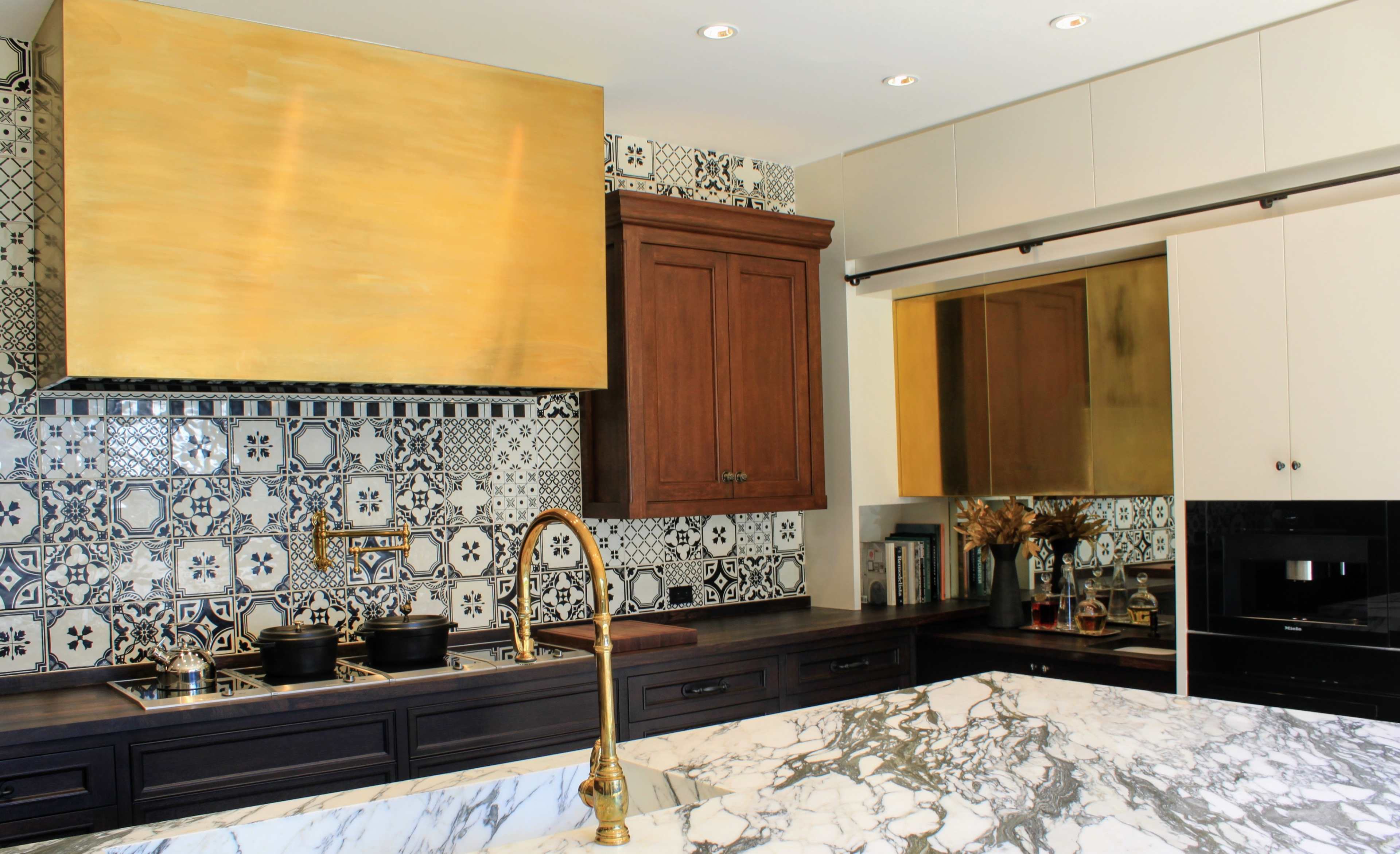 The kitchen features a marble island, a gold vent hood, and patterned tiles on the walls.