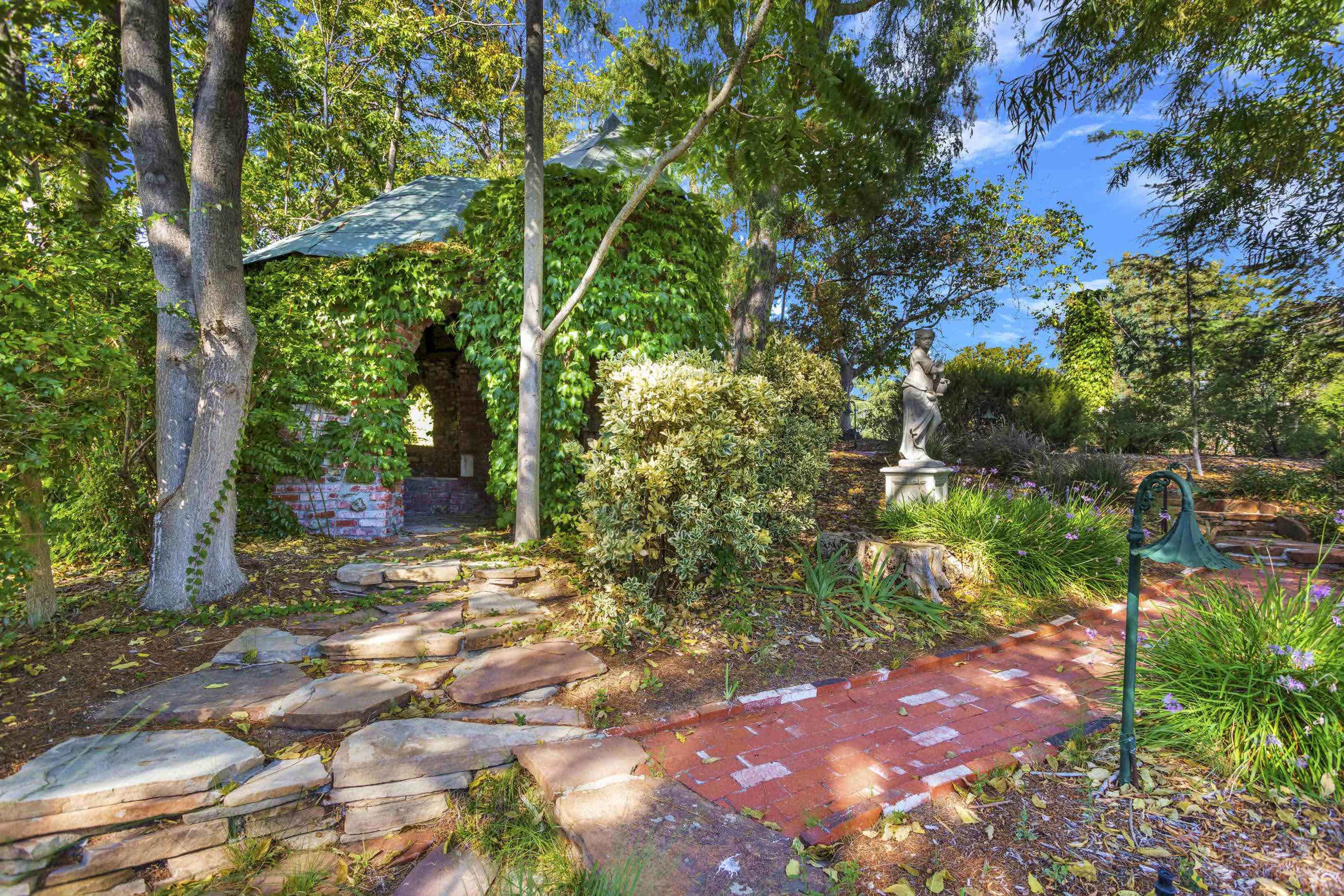 A stone pathway leads to a small, ivy-covered structure surrounded by trees and colorful foliage.