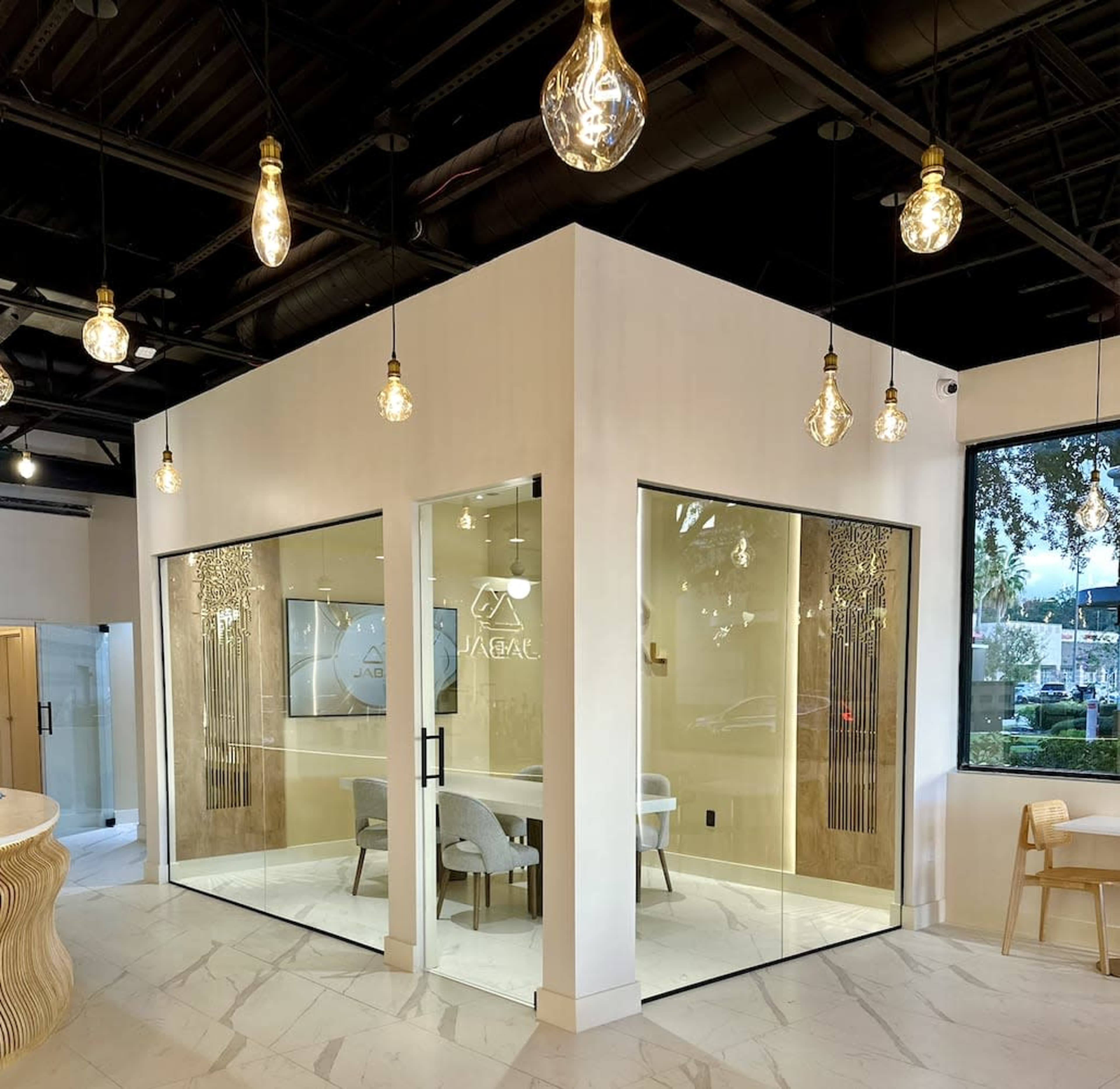 The image shows a modern office space with glass-walled conference rooms, a light-colored interior, and pendant lights hanging from the ceiling.