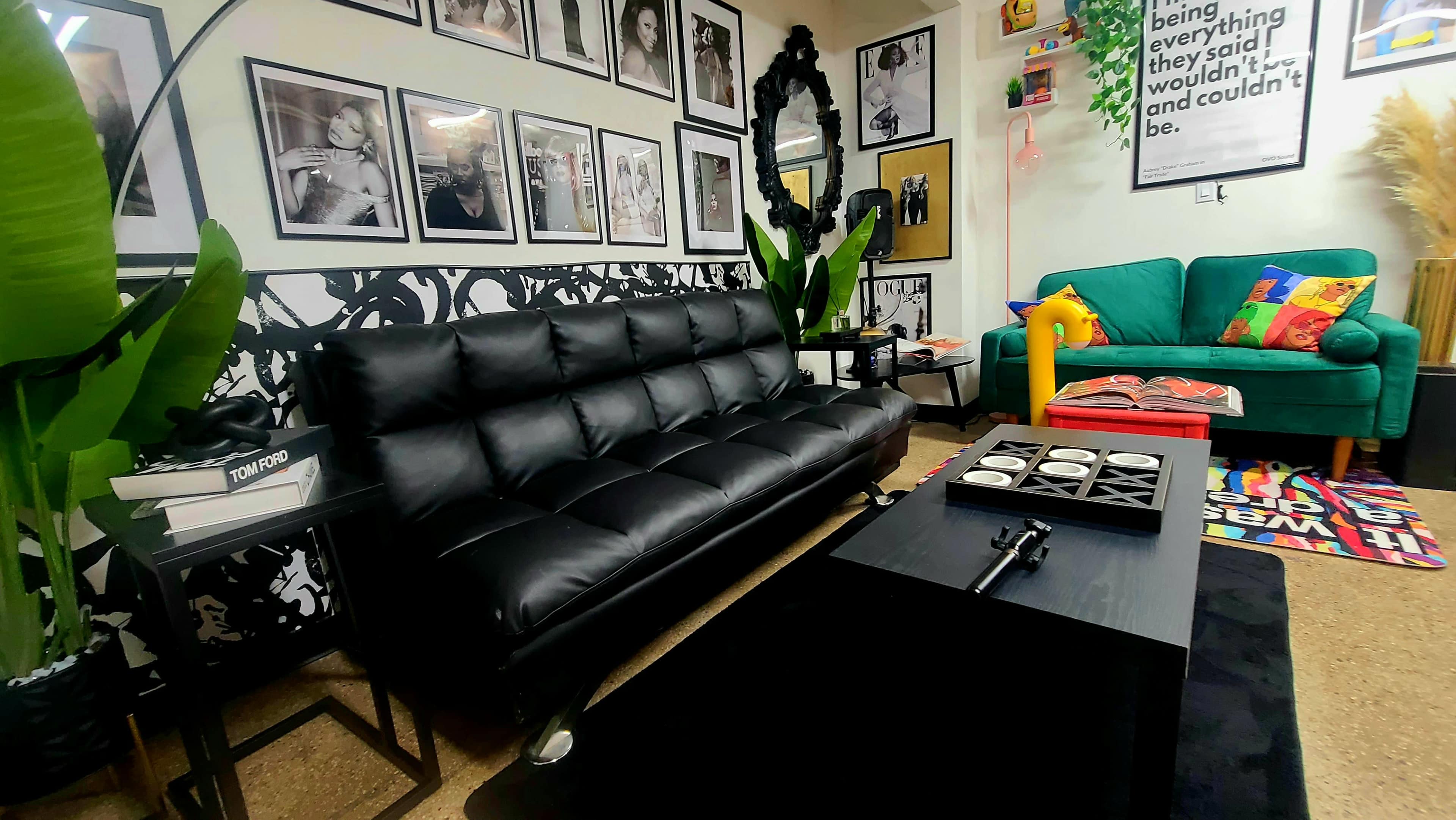 A modern living room features a black sofa, colorful armchair, framed art on the walls, and various decorative items.