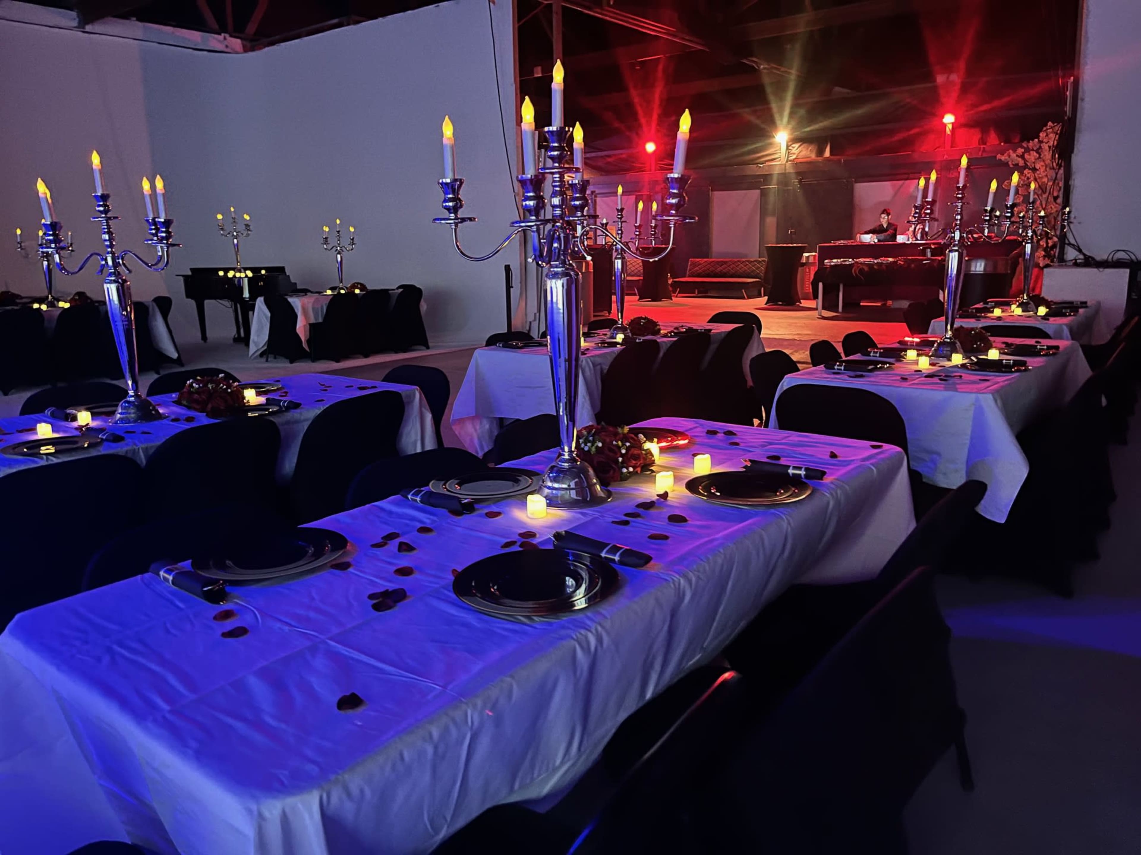 The image shows elegantly set tables with candelabras and decorations, arranged in a dimly lit room prepared for an event.
