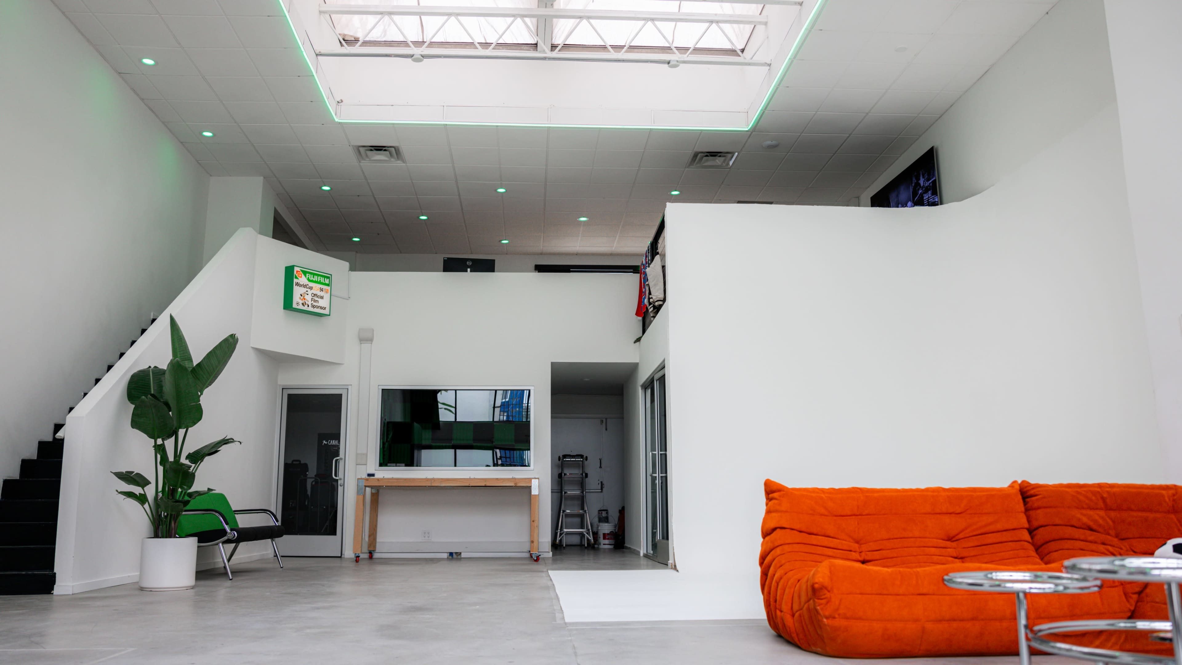 A spacious, modern interior with a large skylight, orange couch, and a staircase leading to an upper level.