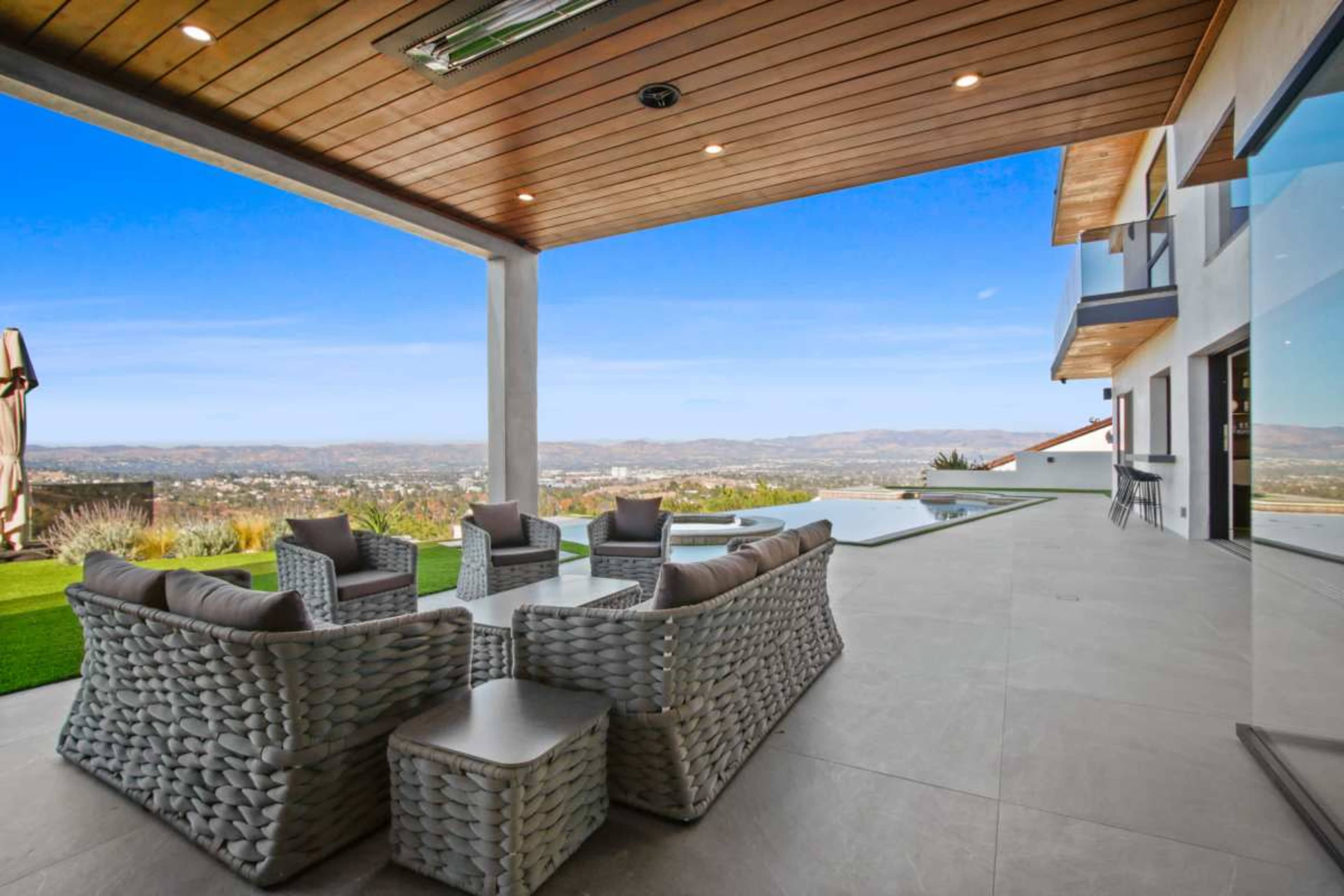 A modern patio features woven furniture and a view of the landscape beyond a swimming pool.