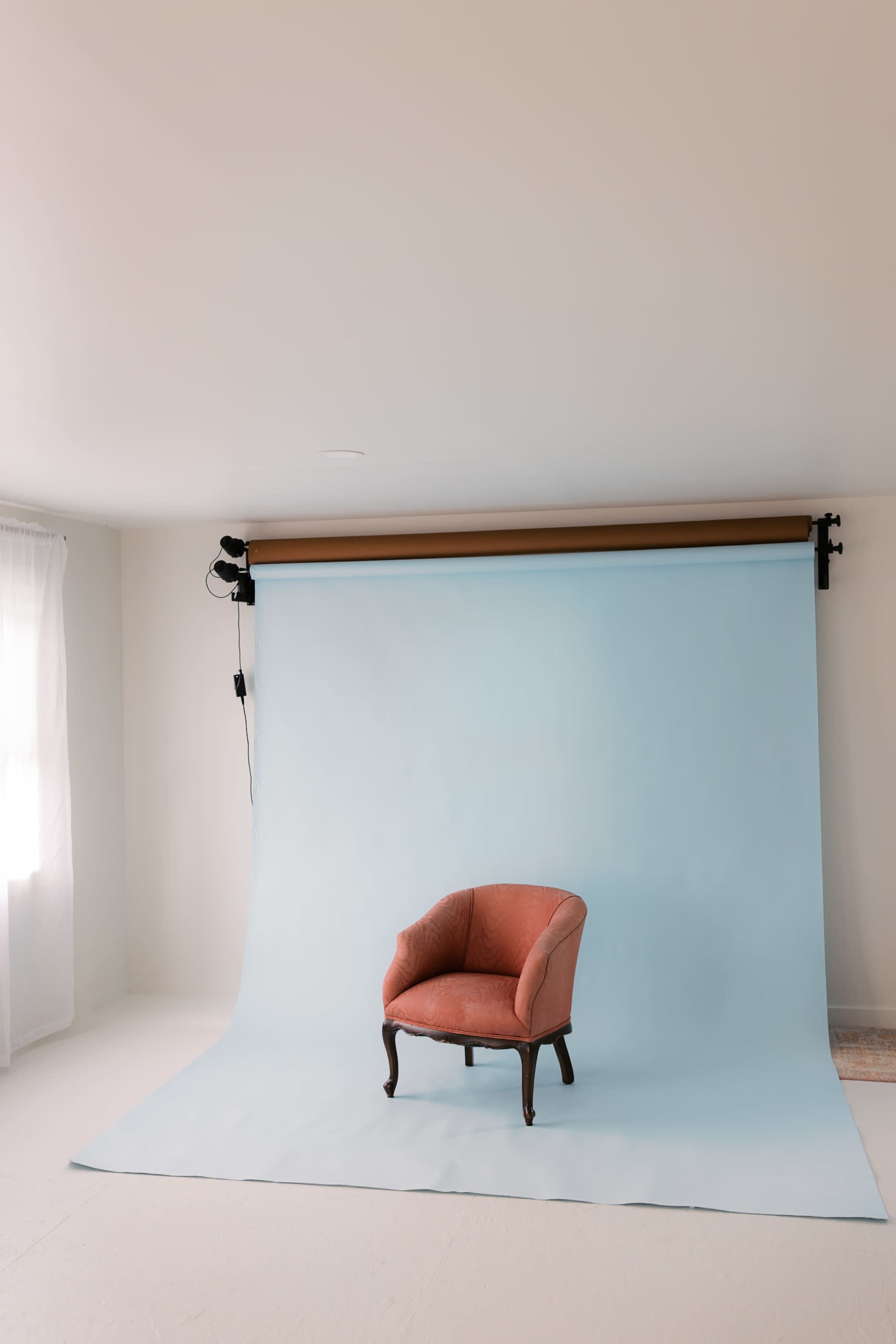 A single pink armchair is positioned in front of a light blue backdrop in a well-lit studio space.