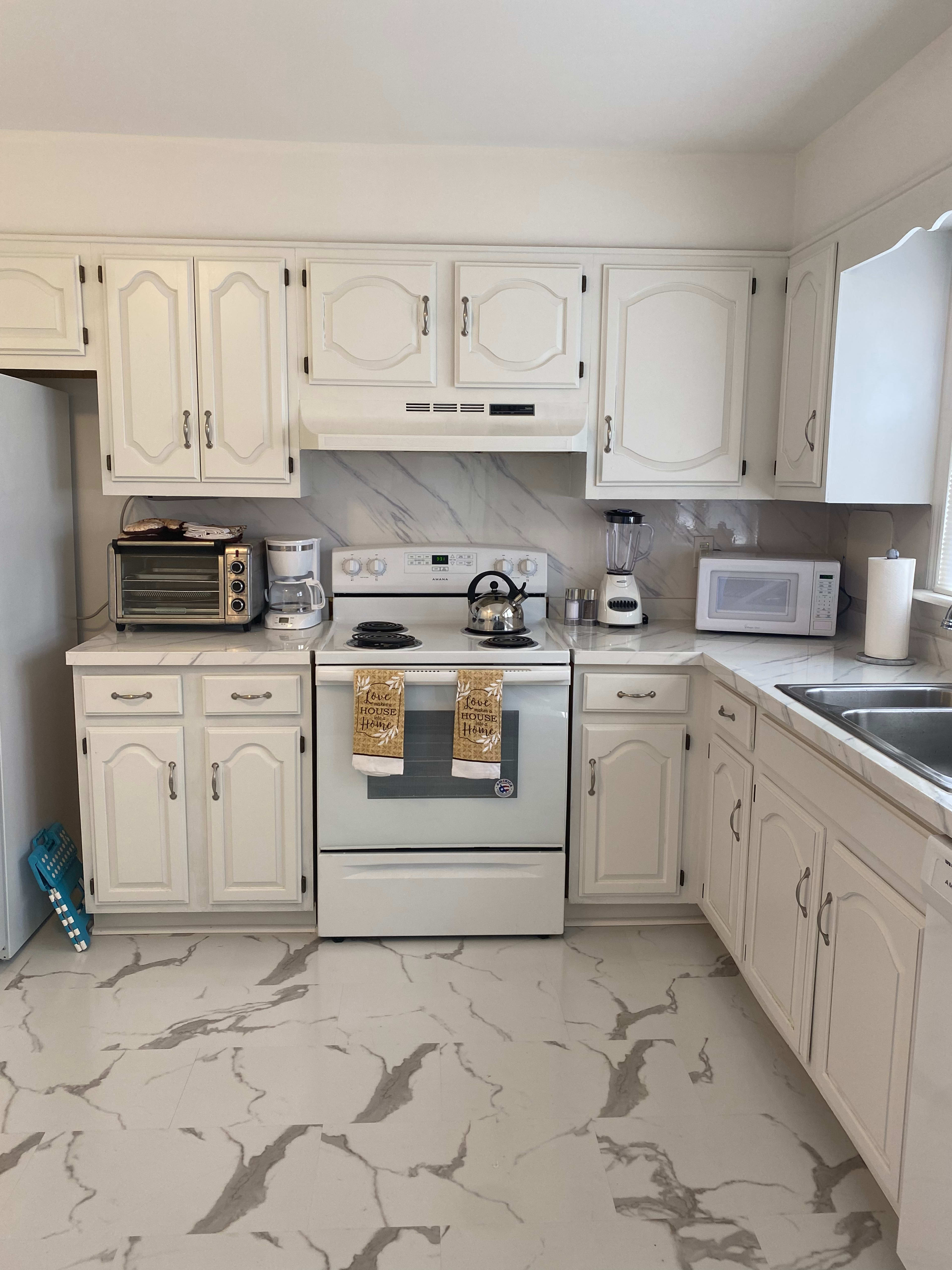 A white kitchen features a stove, microwave, and various appliances arranged around granite countertops and cabinets.