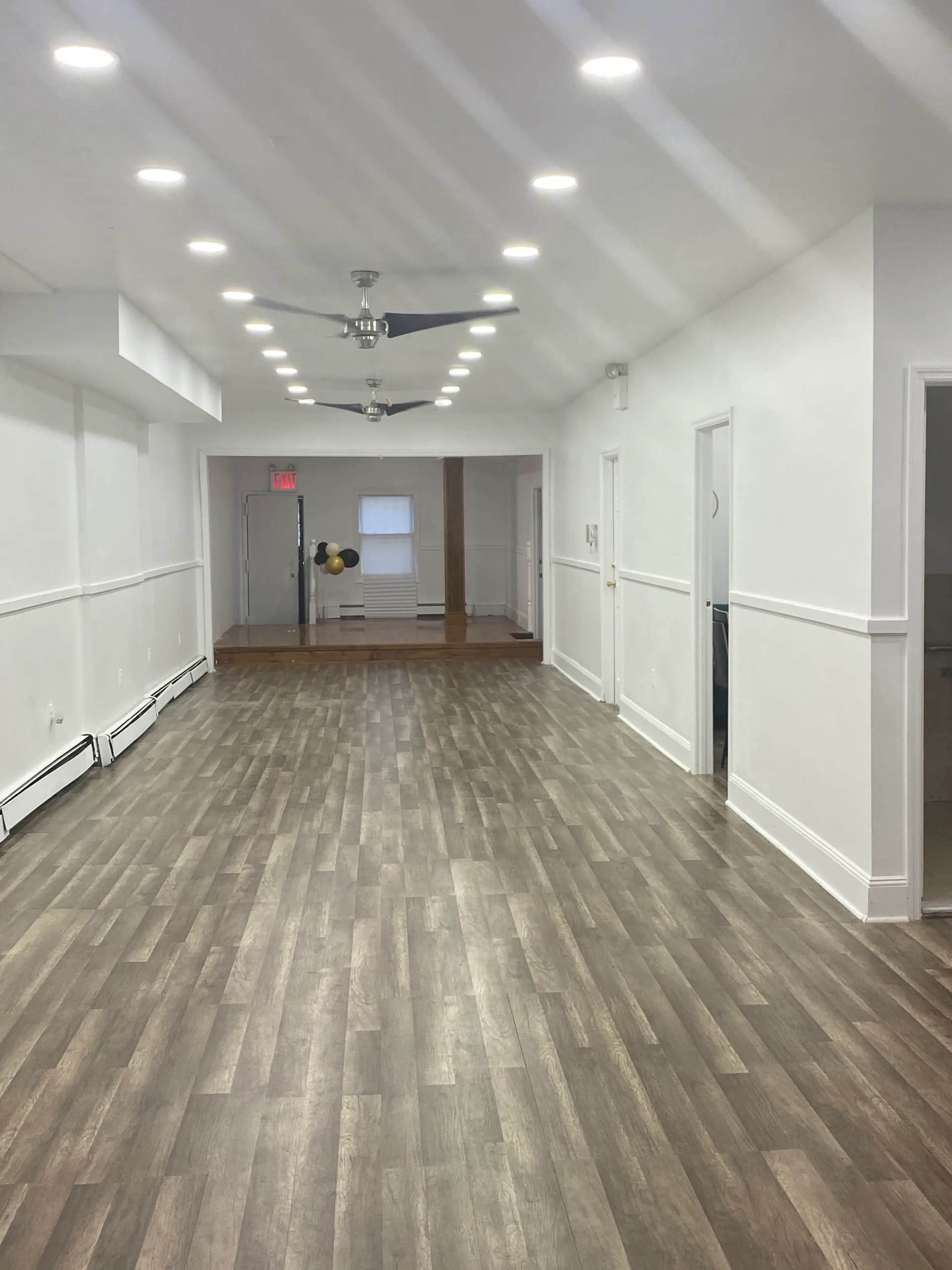 A well-lit, narrow hallway featuring wooden floors and a ceiling fan, leading to multiple doorways at either end.