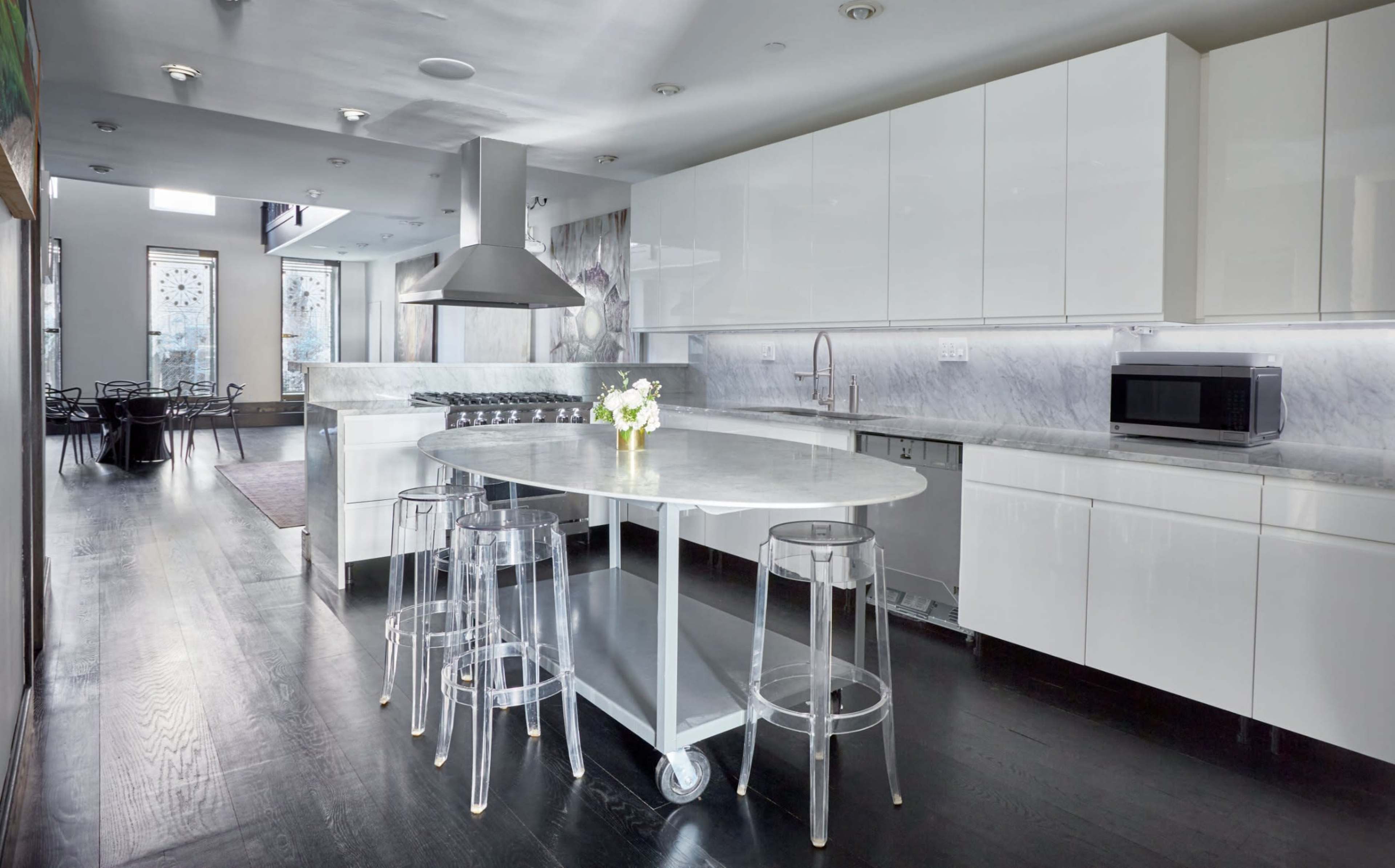 A modern kitchen with sleek white cabinets, a marble countertop island, and clear acrylic bar stools.