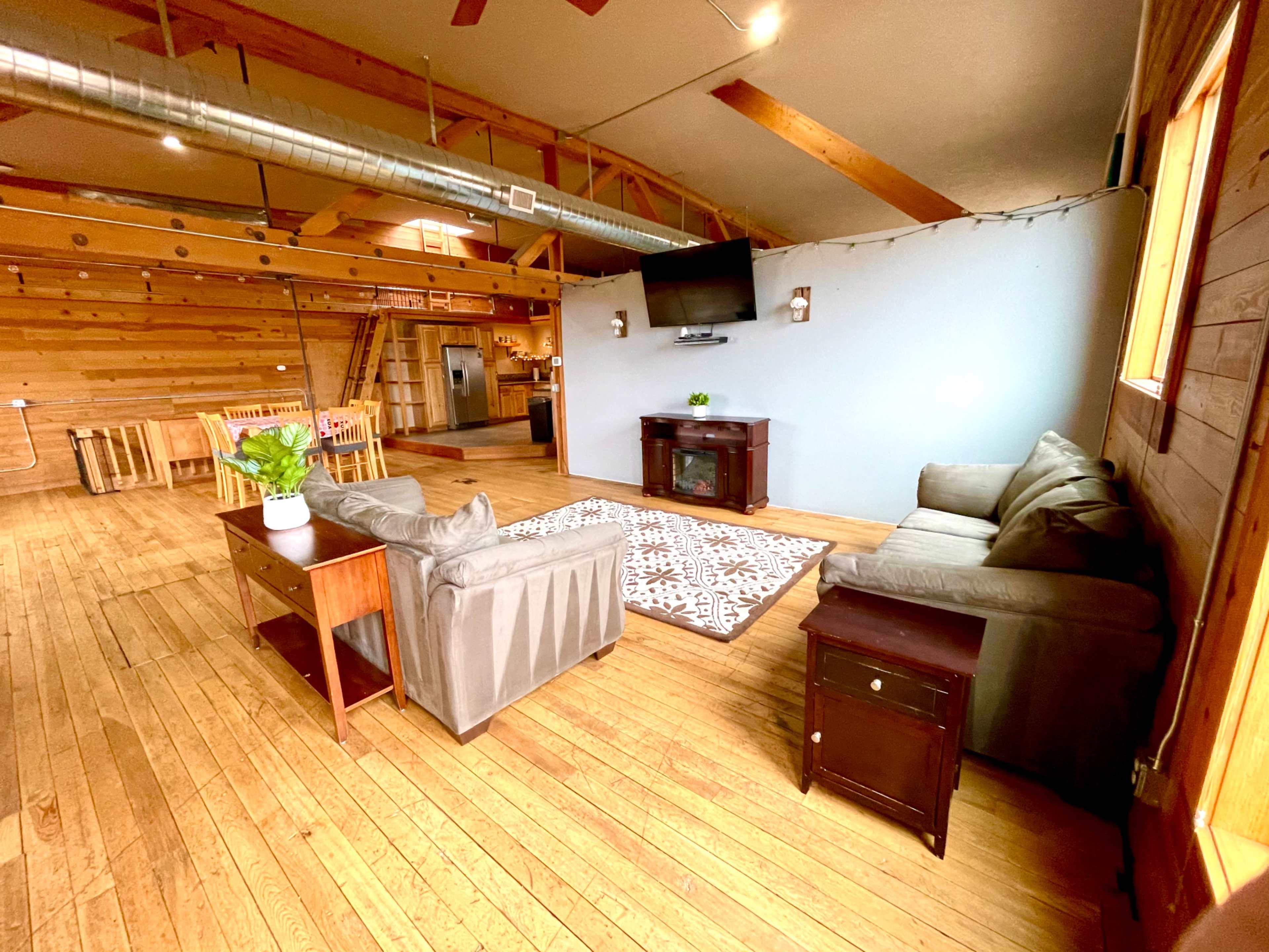 A spacious living area with two sofas, a coffee table, and a television mounted on the wall, surrounded by wooden walls and flooring.