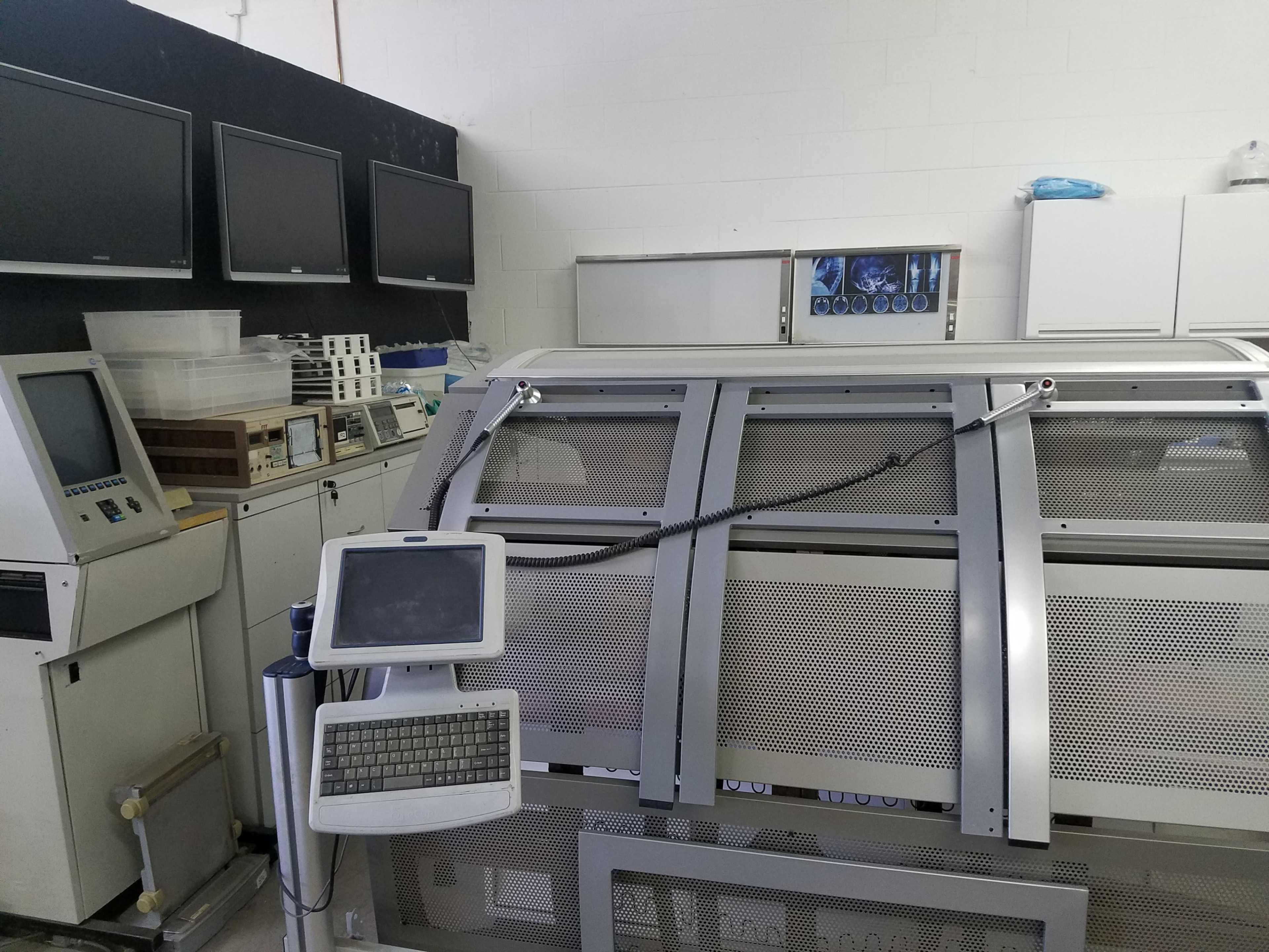 A laboratory or medical room with a large machine surrounded by monitors and a control panel.
