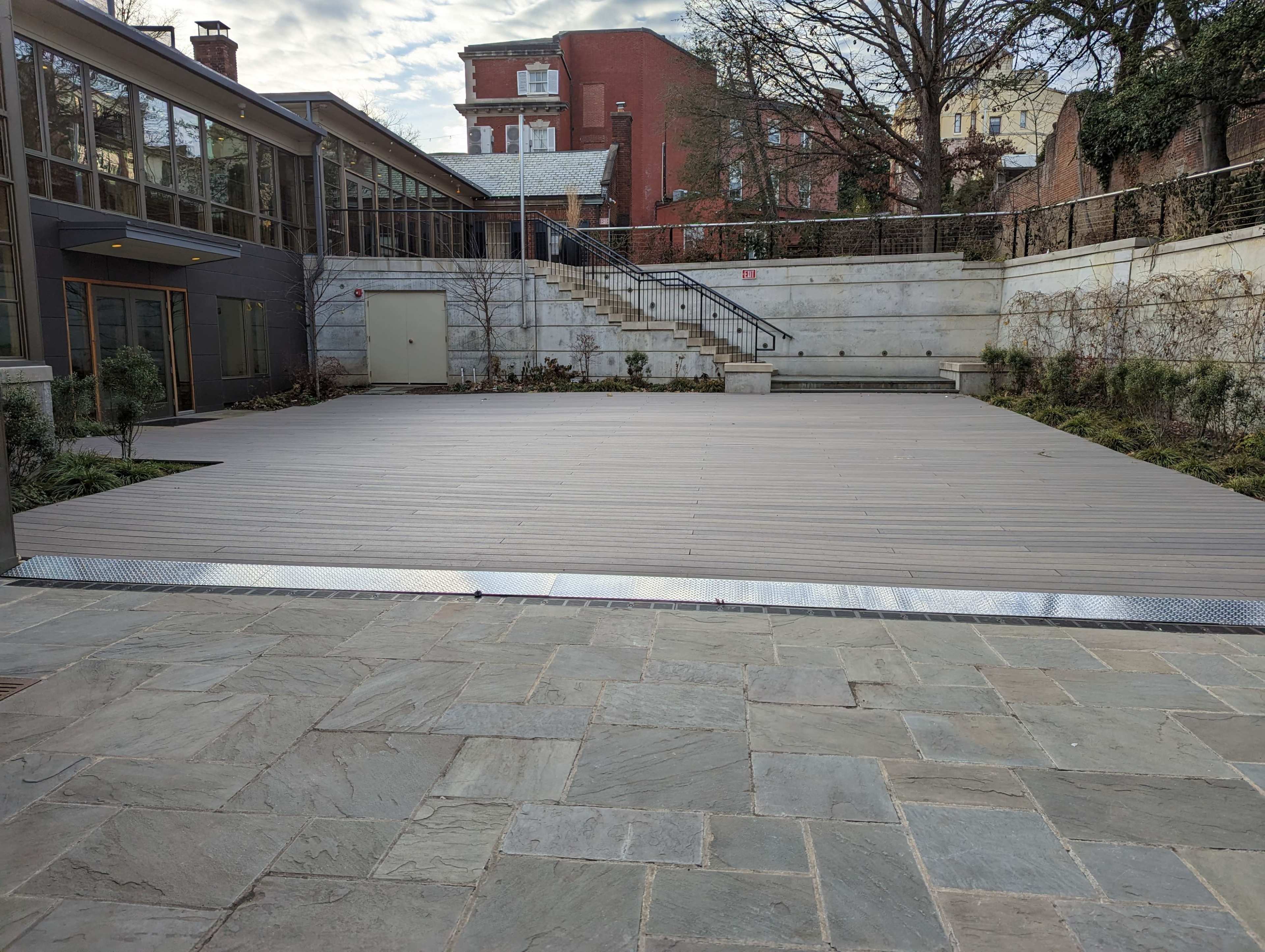 A wooden deck area enclosed by stone walls and steps, with a building in the background.