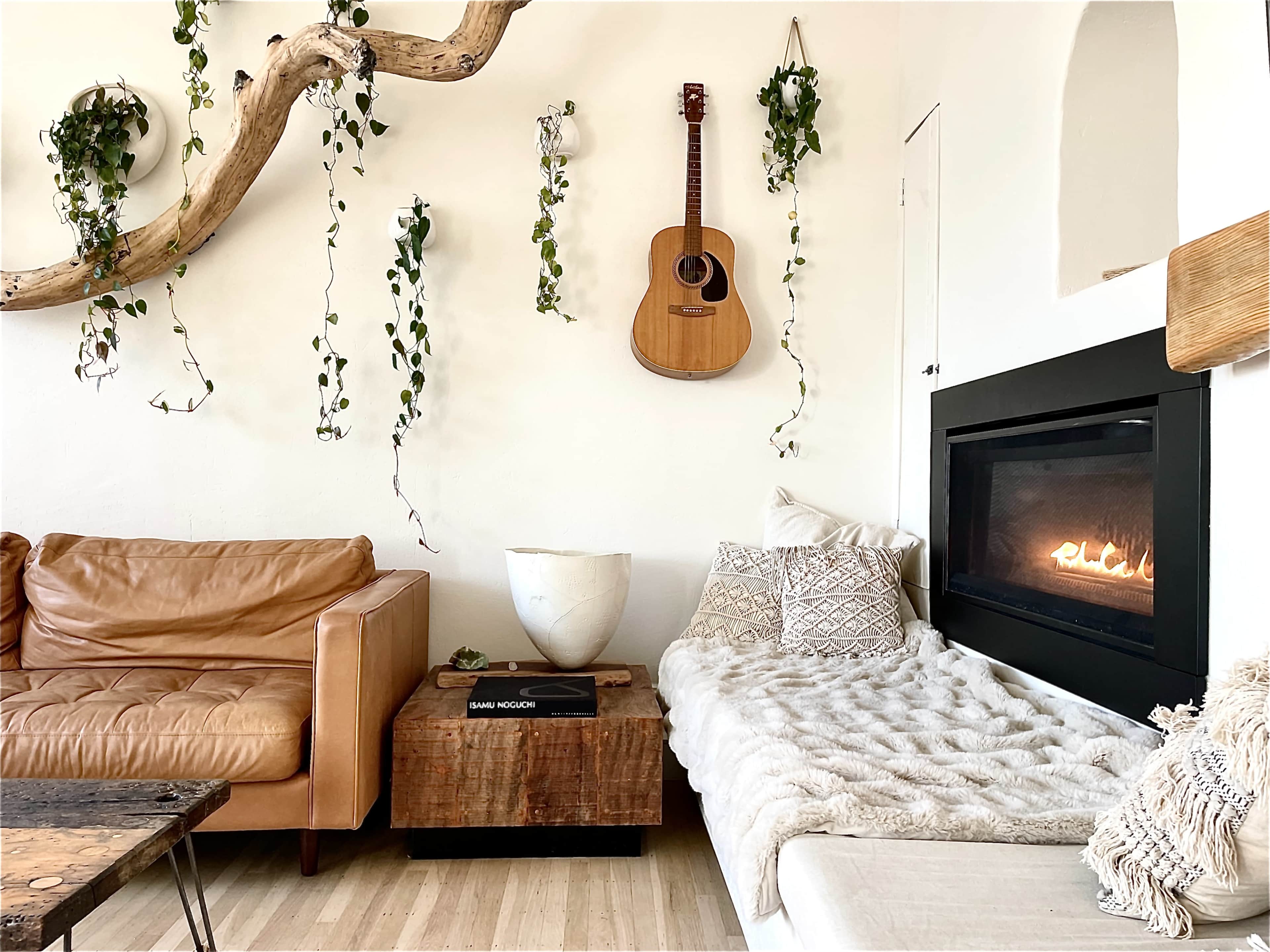 The image shows a cozy living room with a brown leather couch, a white sofa, a wooden coffee table, an acoustic guitar mounted on the wall, and a modern fireplace.