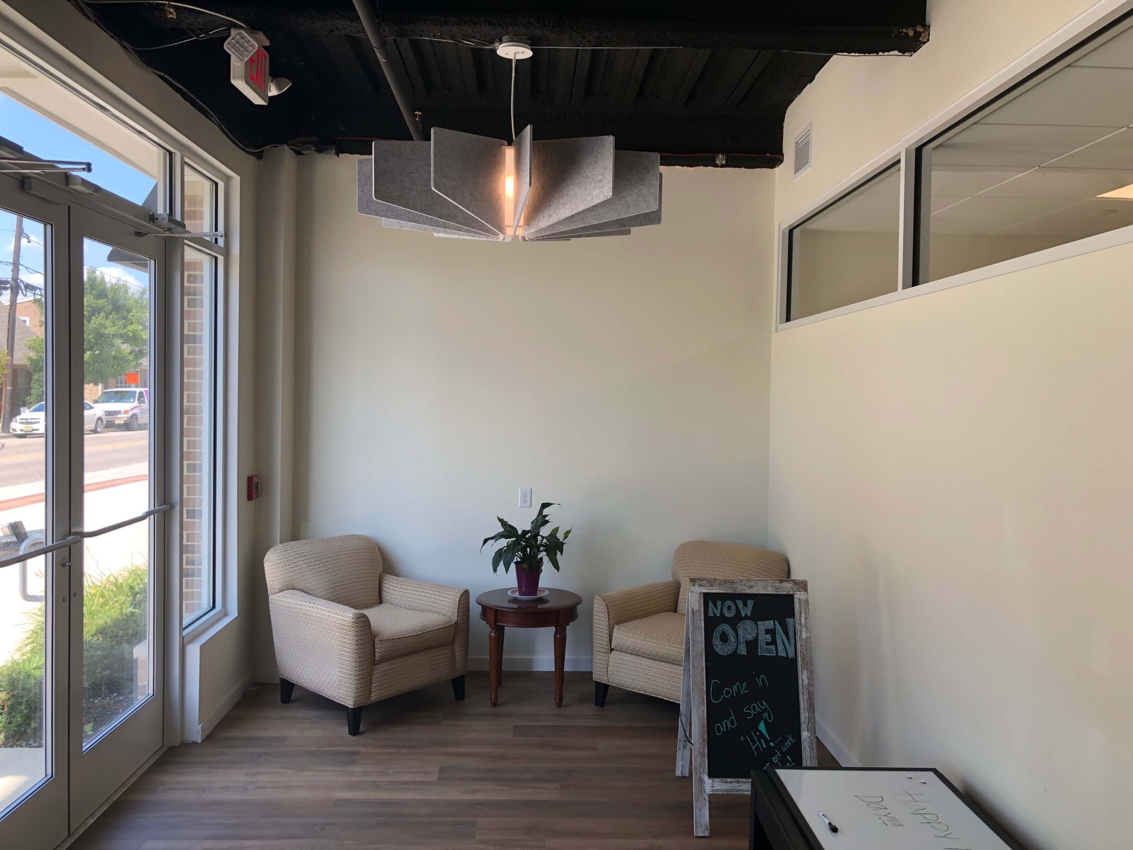 A small indoor seating area with two chairs, a table, a potted plant, and a sign that reads "NOW OPEN" on a chalkboard.